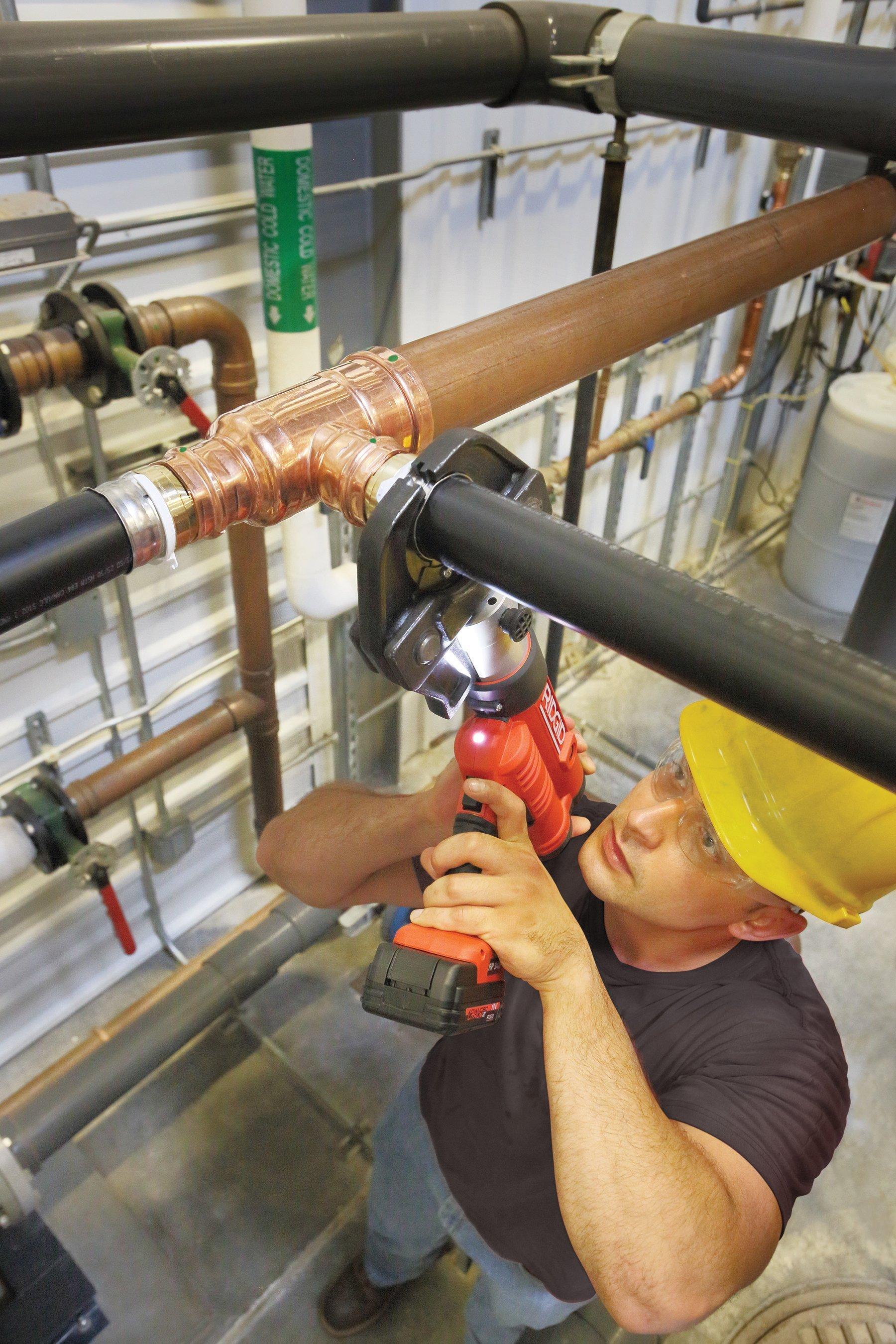 A contractor uses a press tool to connect overhead pipe fittings.