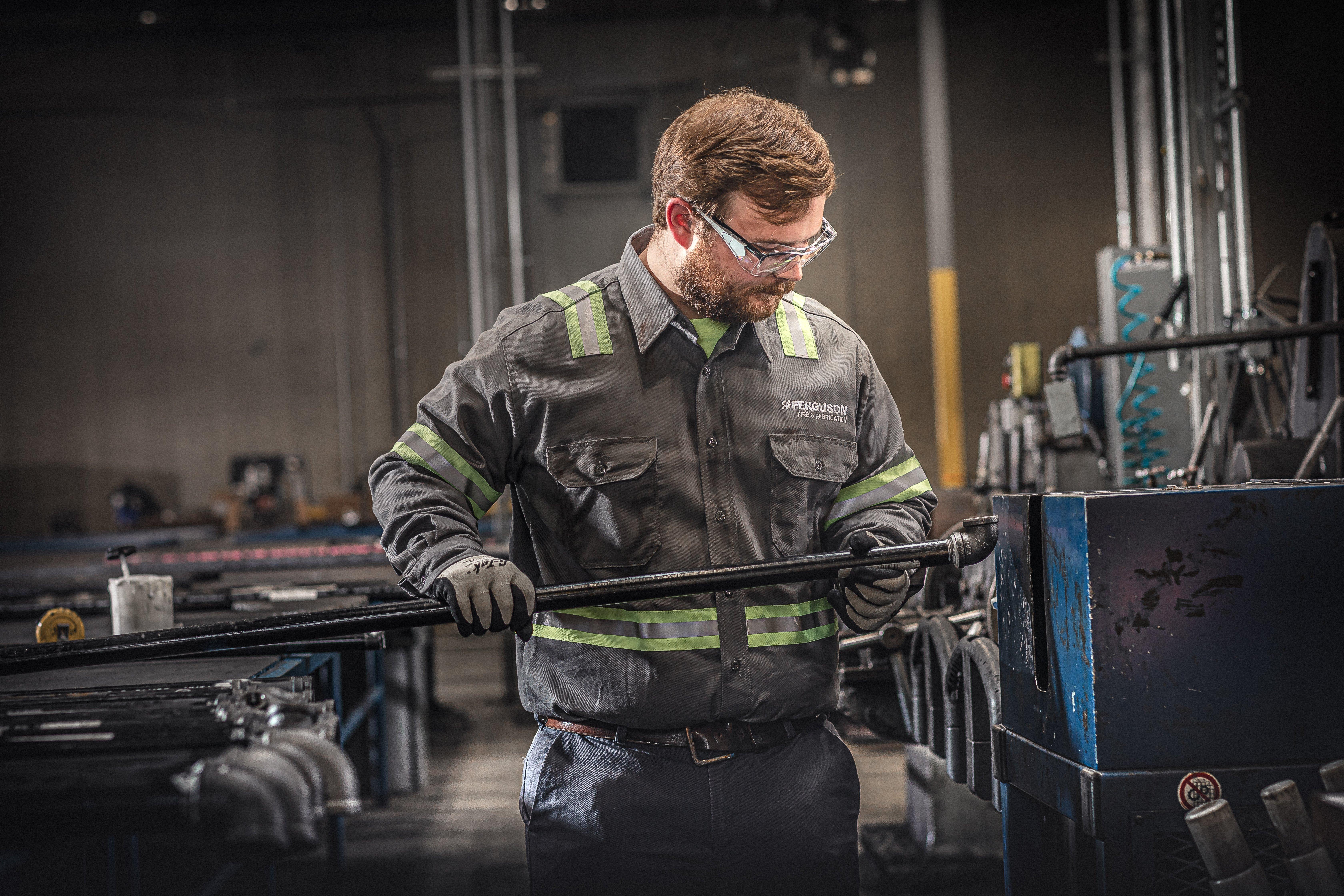 A Ferguson associate examines a pipe next to a machine in a Fire & Fabrication facility.