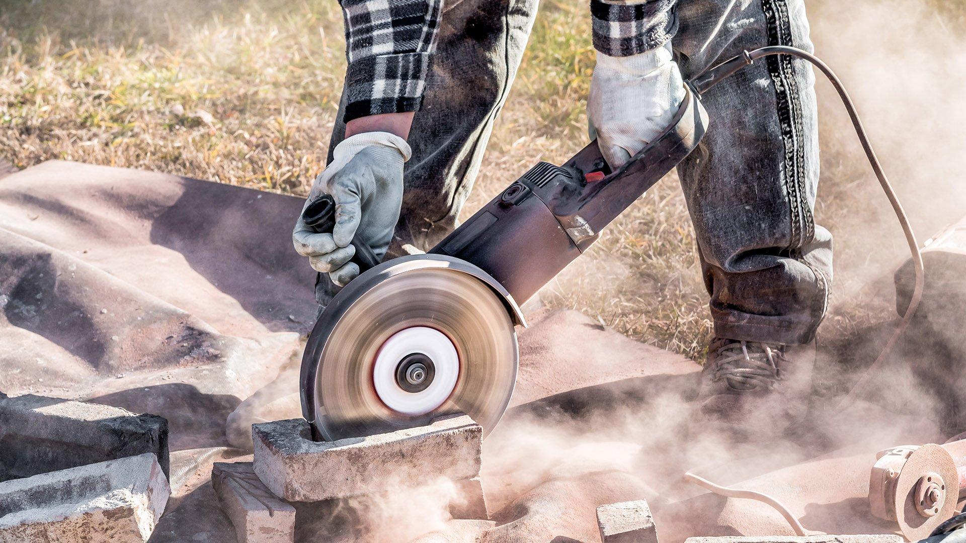 A worker wearing white protective gloves cuts bricks with a circular electric saw.