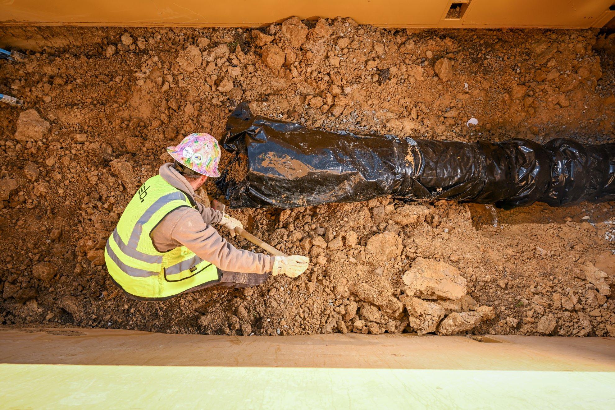 A contractor digs in an excavation around an underground pipe.