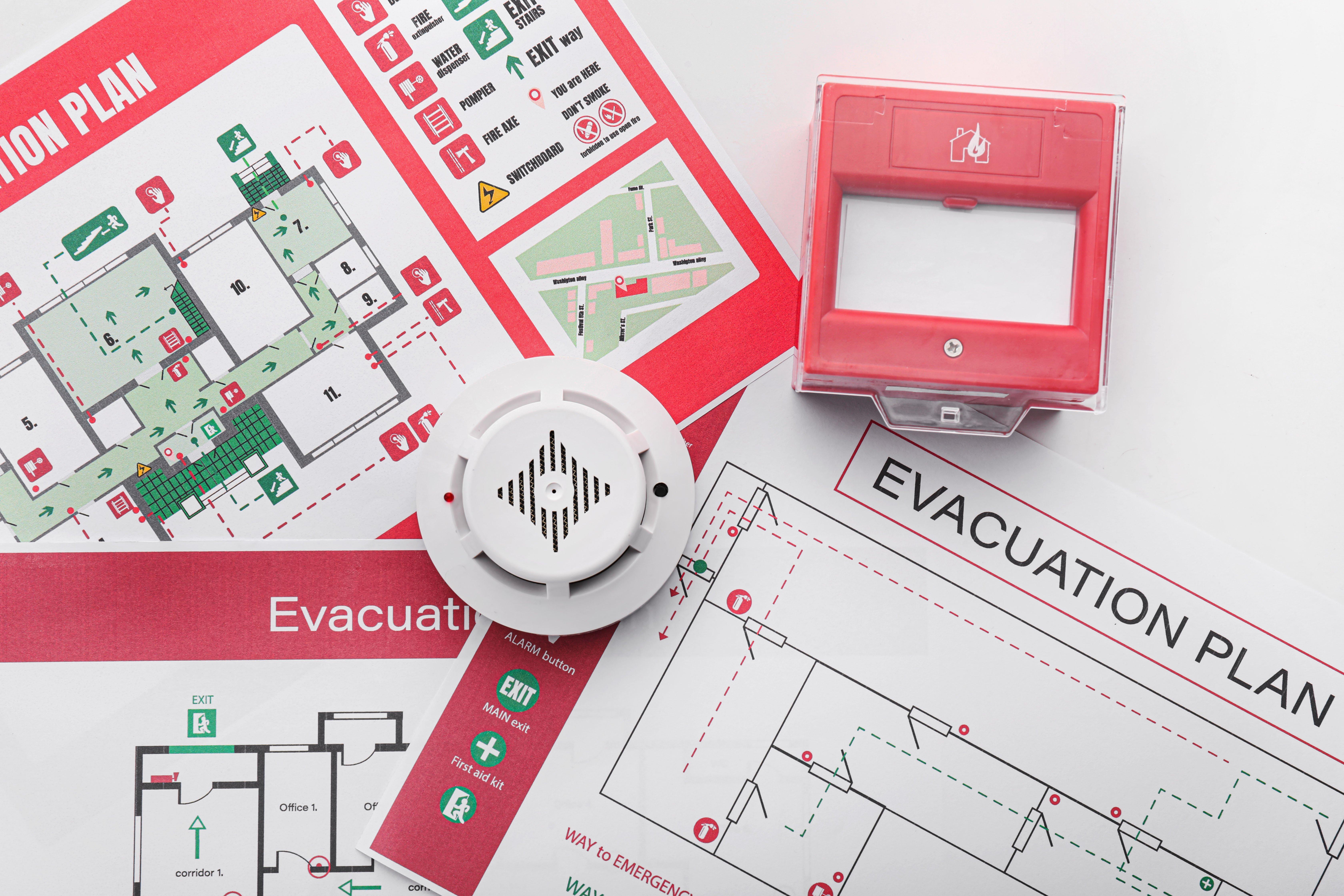 Evacuation plans and smoke alarms lie on a white table.