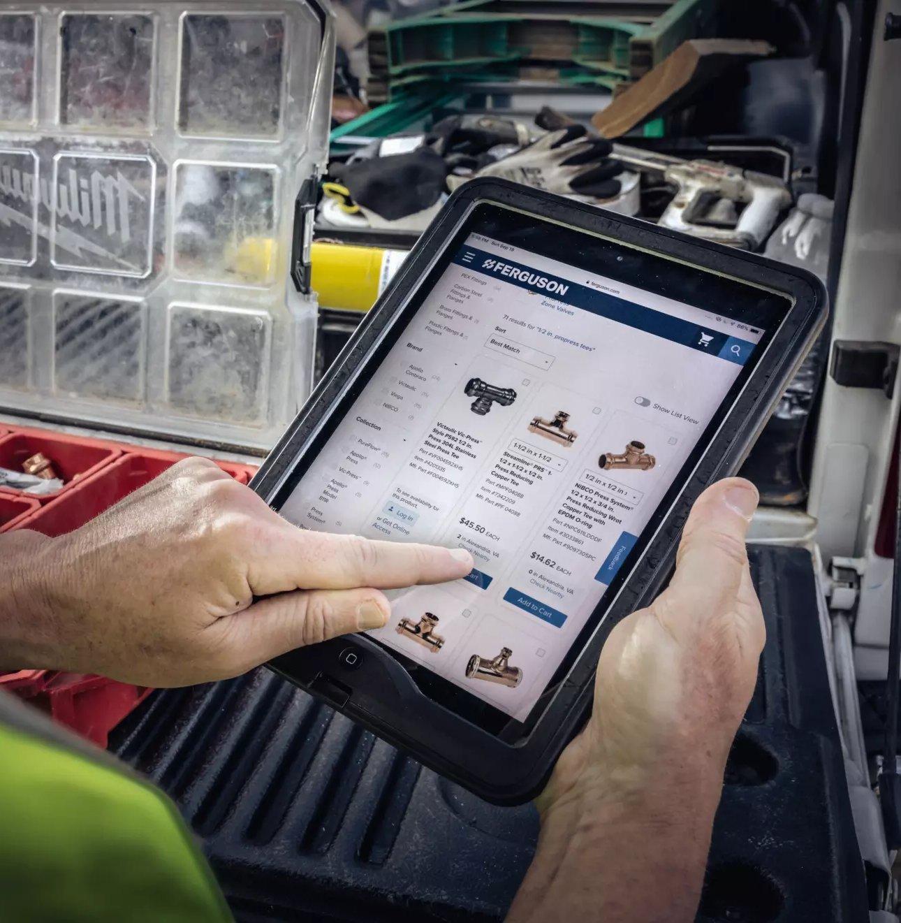 A tradesman browses ferguson.com on a tablet while standing outside truck.