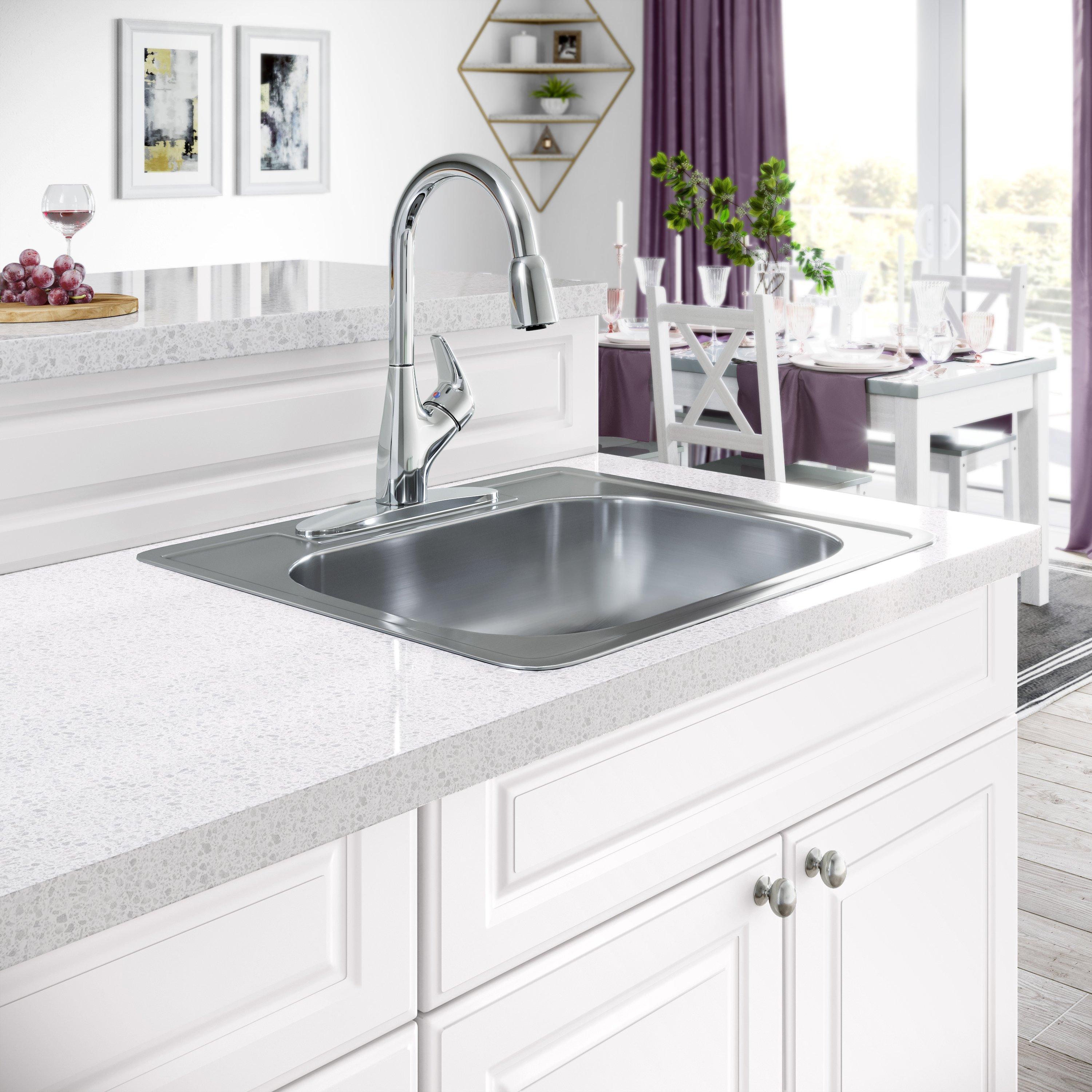 A stainless steel, single-handle pull-down kitchen faucet and sink are in focus in a white kitchen with an island and dining table in the background.