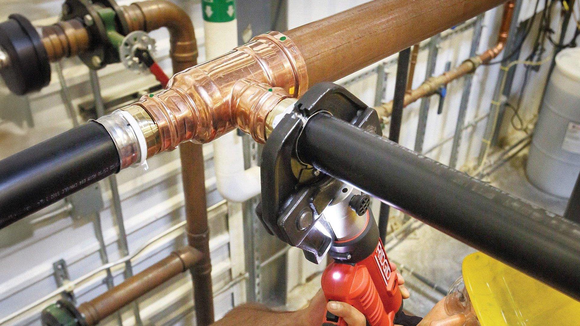 Worker in hardhat uses press fitting on pipe in building.