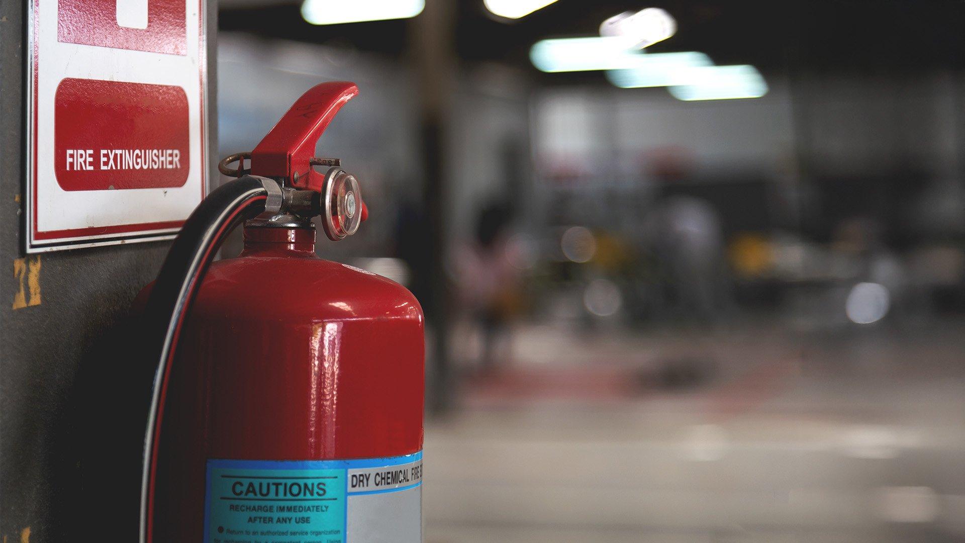 Closeup of red fire extinguisher with soft-focus and overhead lighting in the background