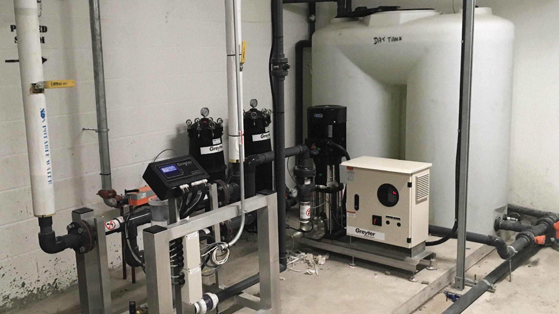 Another type of Greyter commercial graywater reuse modules installed in a commercial space, showing a digital display and other modules, including a large tank marked as “day tank.”