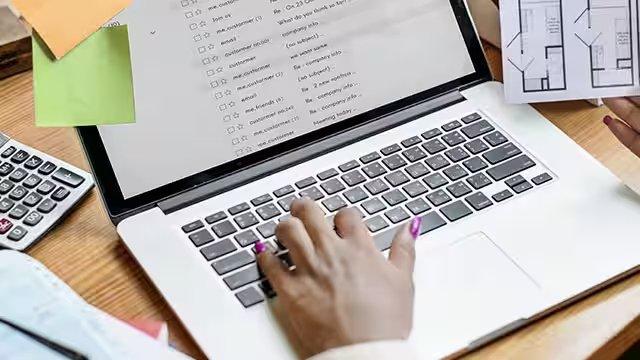 A woman types on a laptop and reviews a room layout.