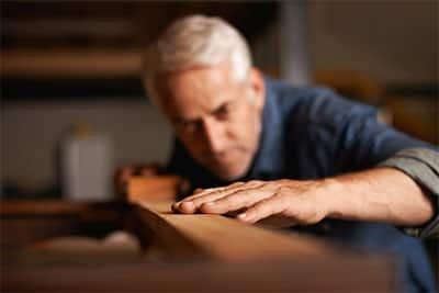 A man leans over a piece of lumber to examine its lines.