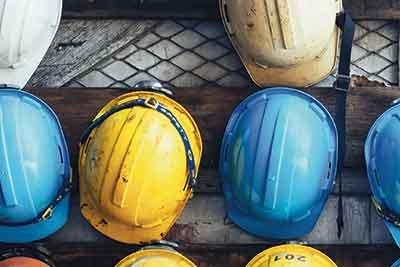 A row of different-colored hard hats hang on a wooden slat.