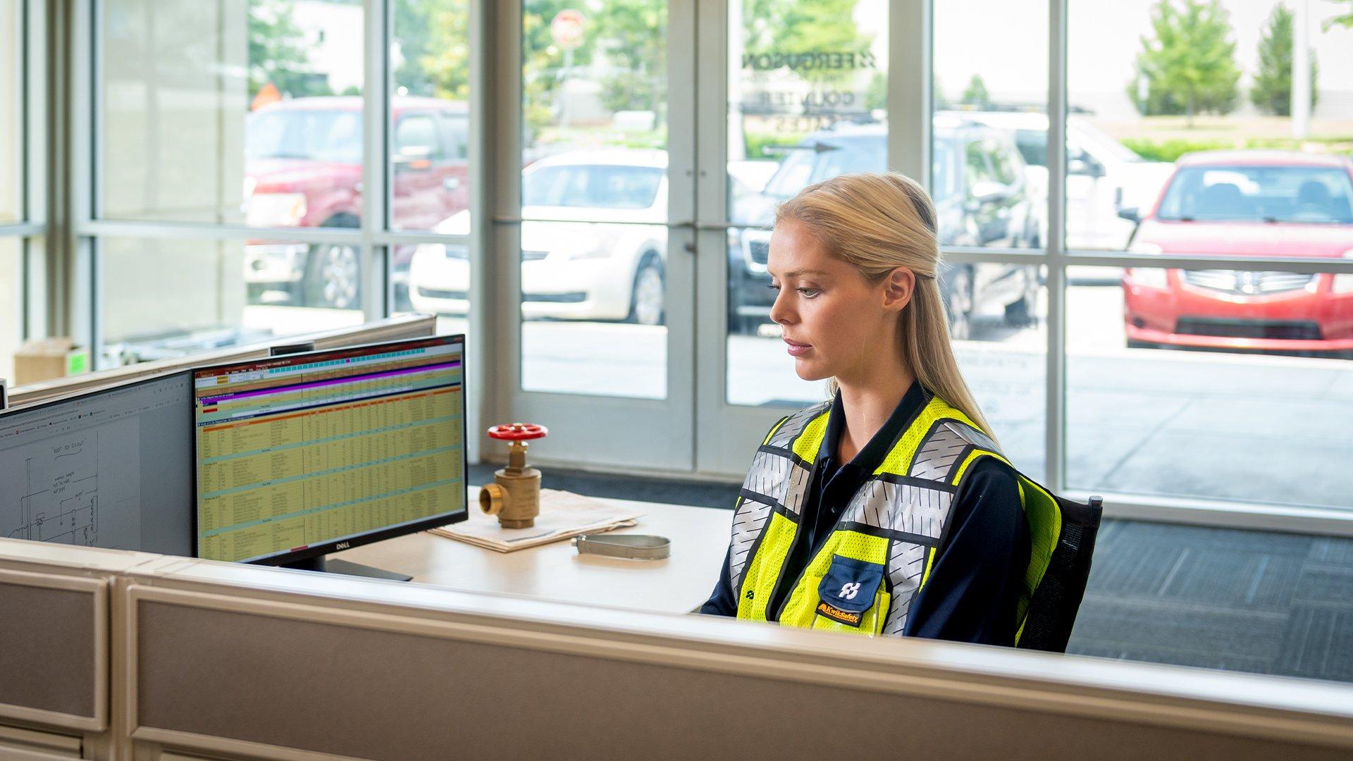 A woman in a high vis vest using a computer with multiple screens.