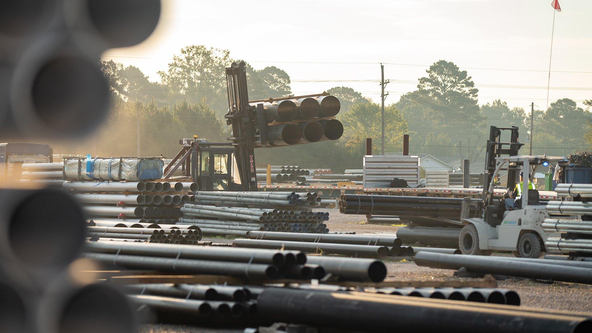 Forklifts carry stacks of pipe through a pipe yard.