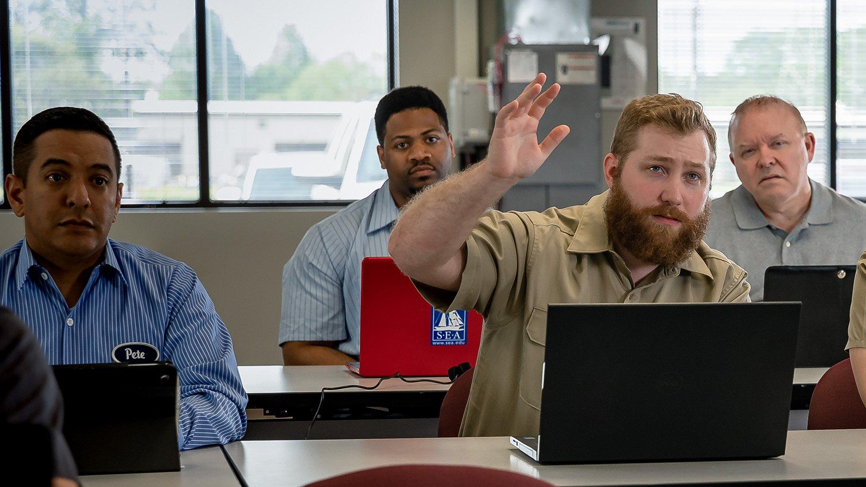 A group of men sit in a classroom with computers.