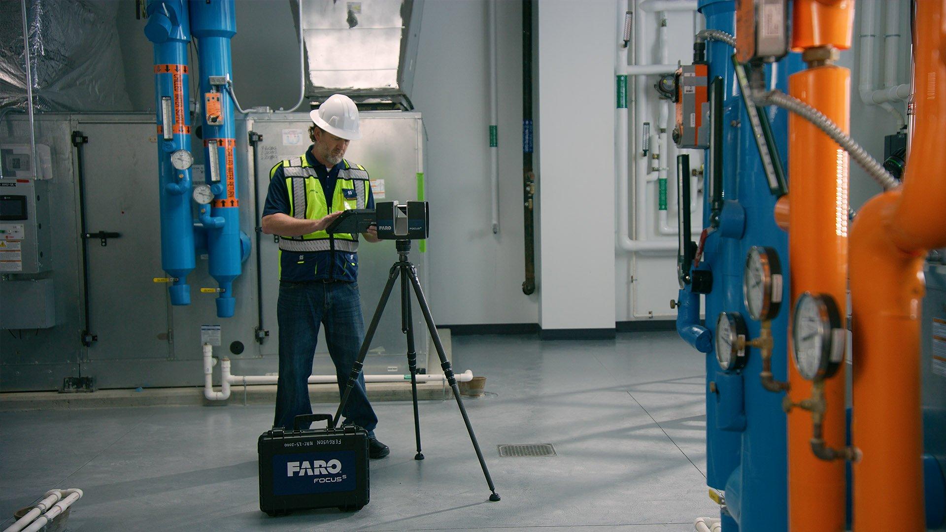A Ferguson associate wearing a reflective vest and a hardhat uses a Faro 3D scanner in a mechanical room.