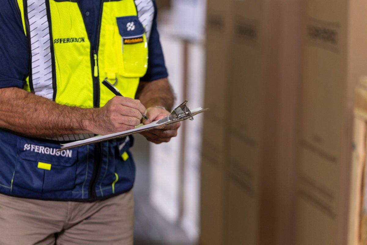 A Ferguson associate in a warehouse writes on a clipboard.