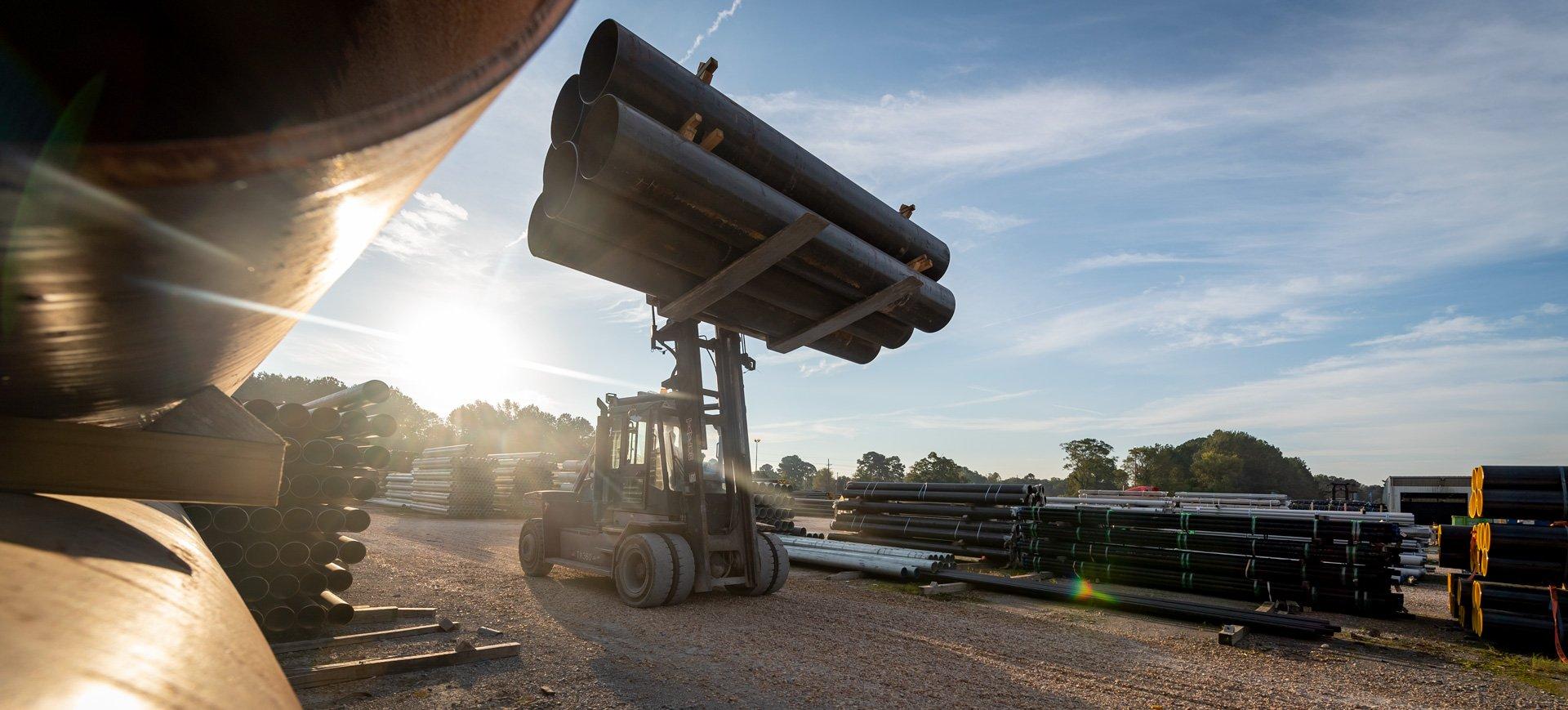 A heavy-duty forklift transports pipe on a jobsite.