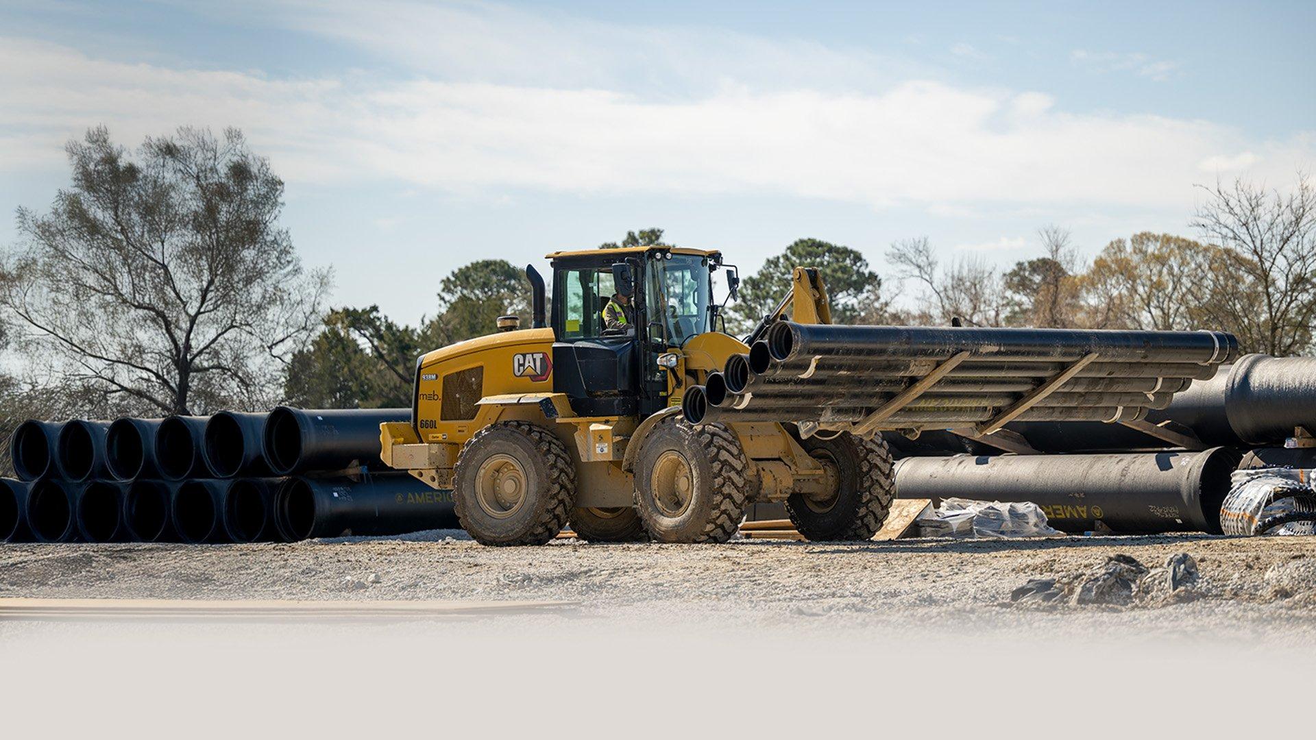 Large, yellow construction vehicle carries pipe bundle on jobsite. 