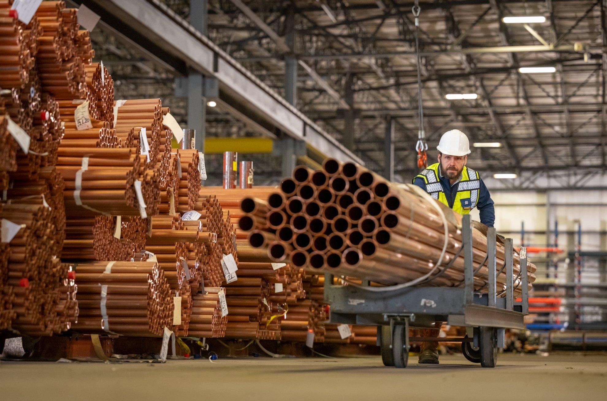 A Ferguson associate in a warehouse moves a stack of pipe on a cart.