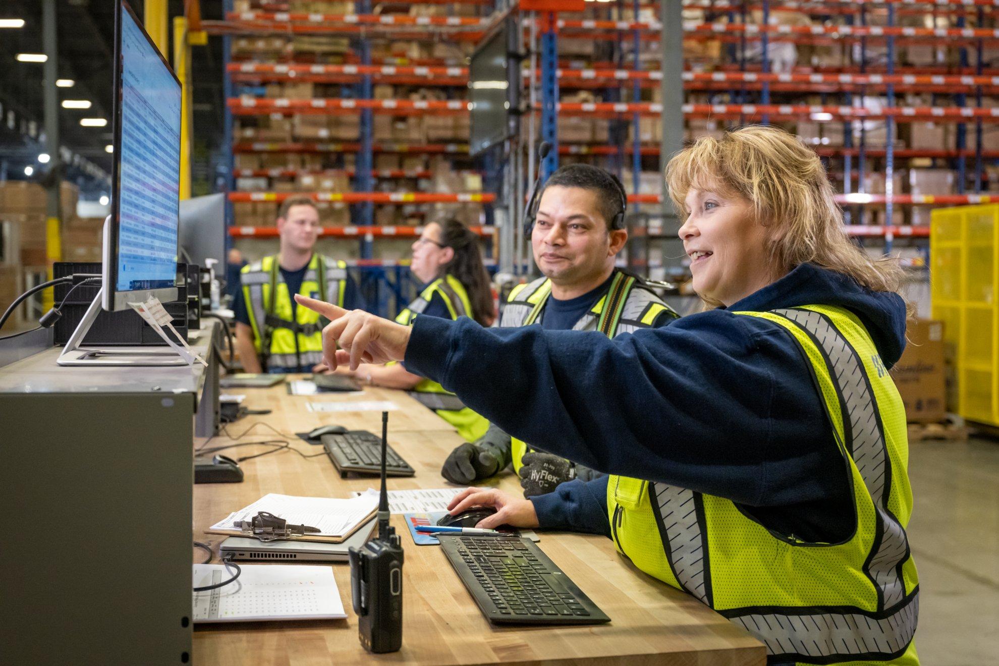 In a Ferguson distribution center, an associate at a desk points to something on her computer screen for another associate.