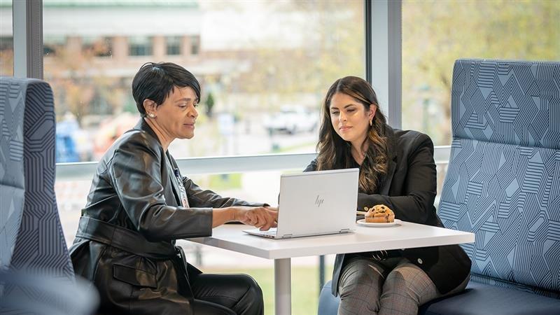 Two business people sit across from each other at a table and look at a laptop together.