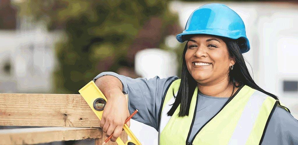 A woman contractor wearing a safety vest holds a level on a jobsite.