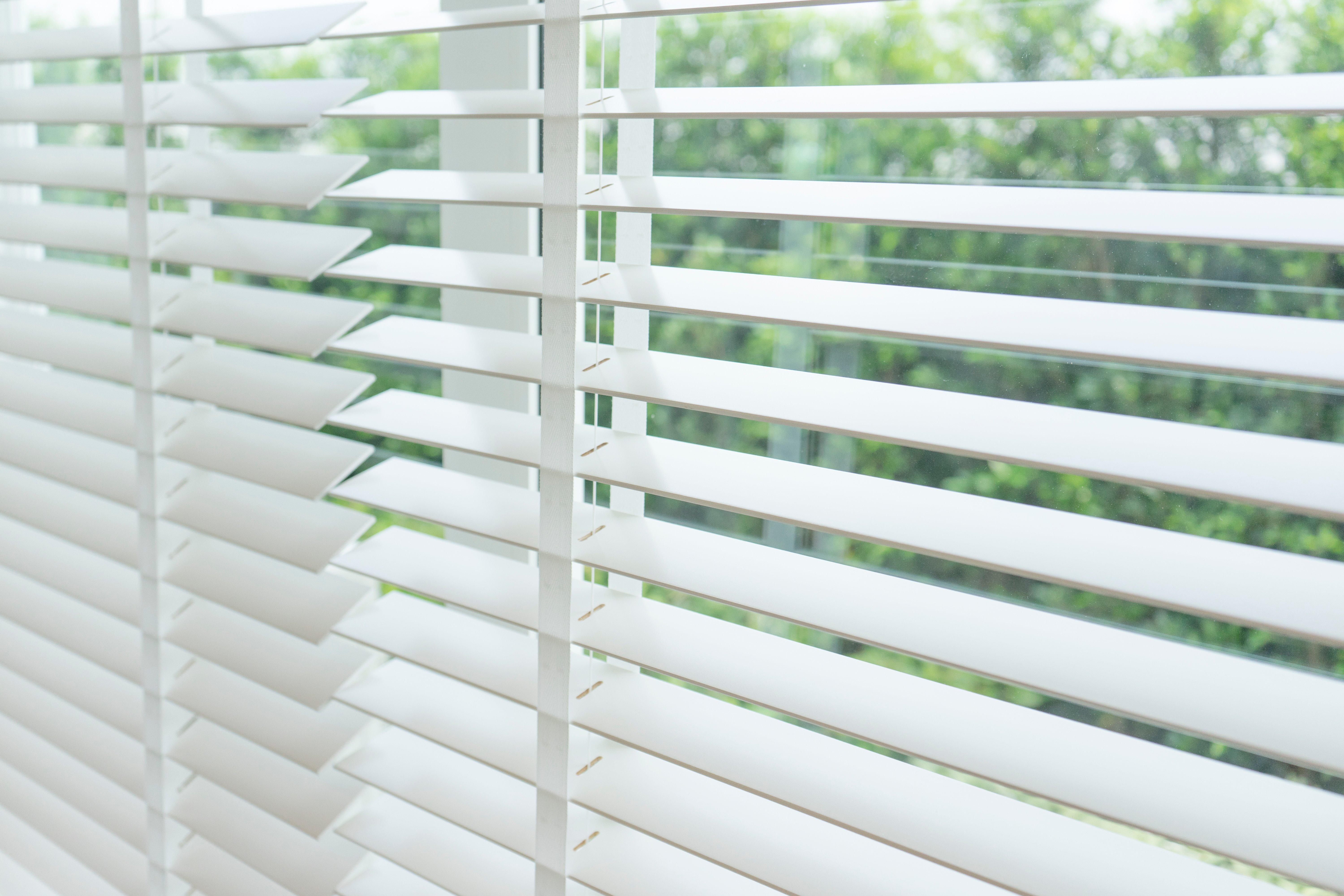 White blinds are opened in front of a window.