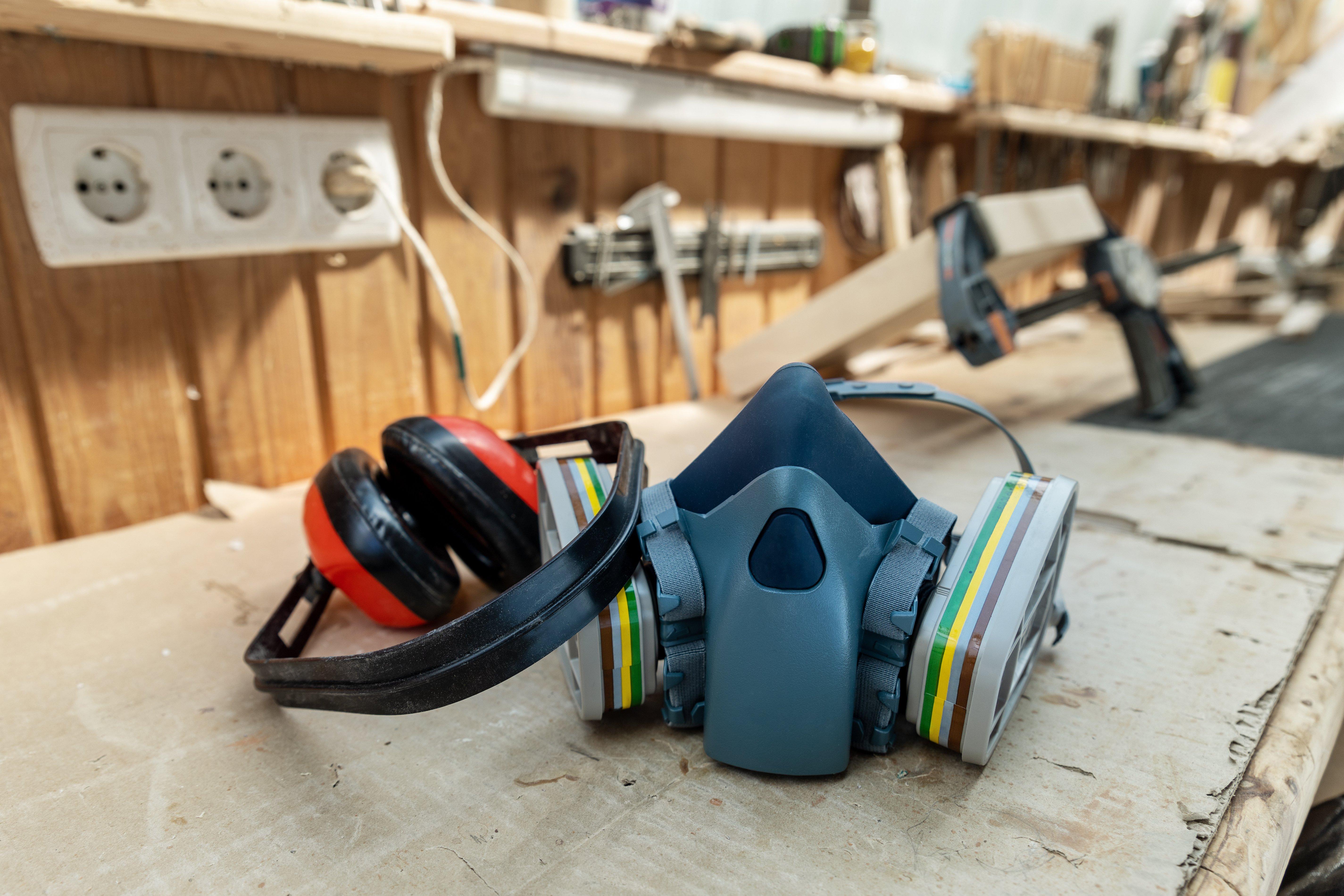 A PPE respirator half face mask and ear protection equipment lie on a wooden carpentry workbench.
