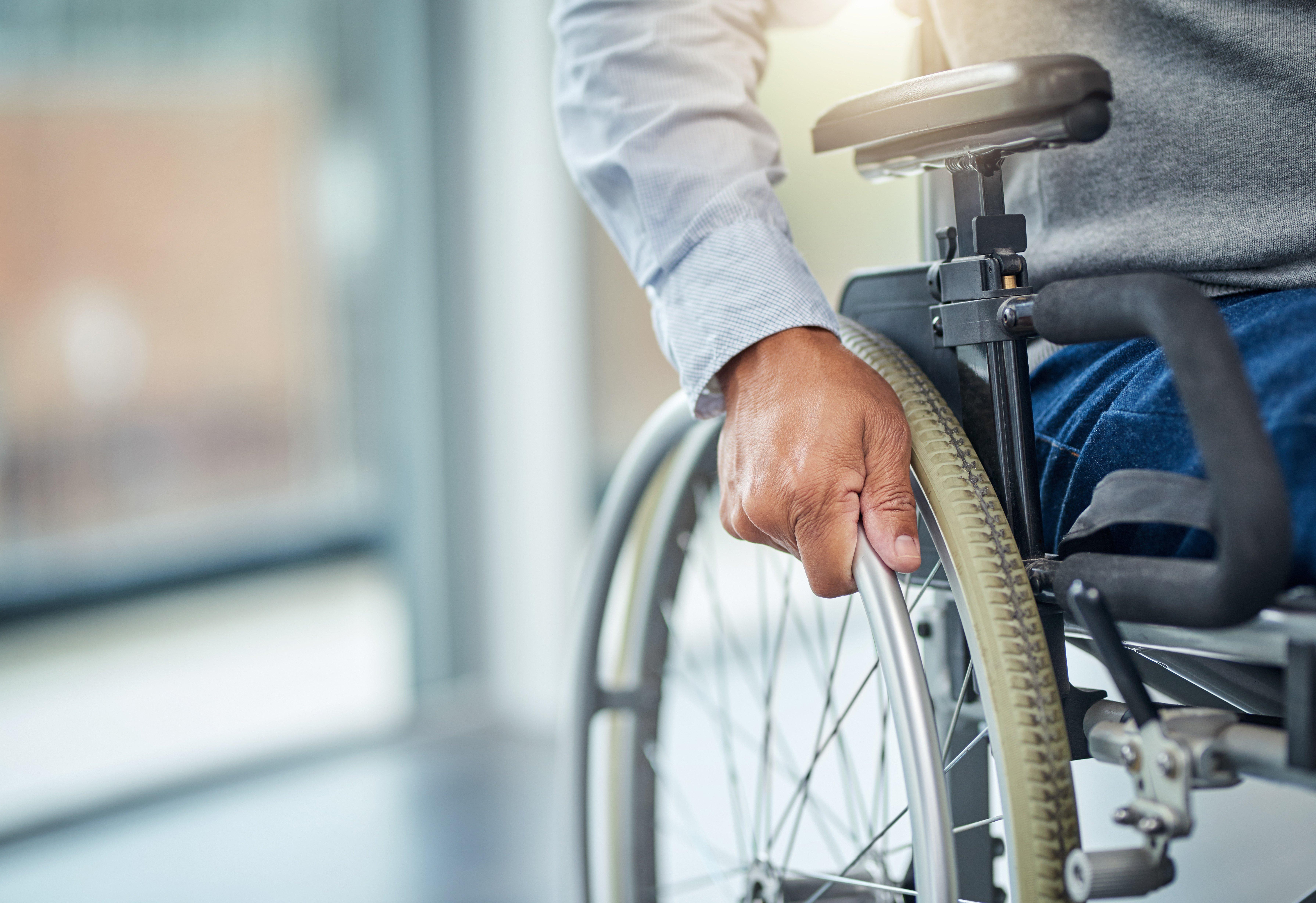 A person’s hand grips the bar on their wheelchair to move forward.