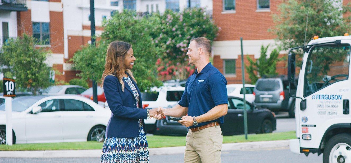 A Ferguson associate shakes hands with a property manager in a parking lot. Boxes of supplies and a Ferguson delivery truck are in the background.