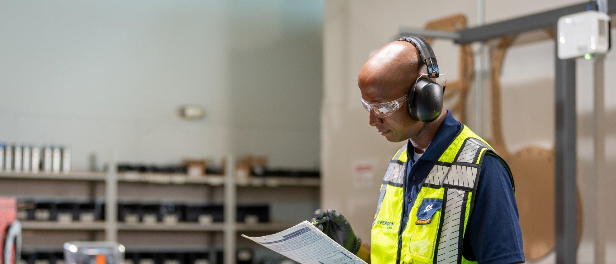 A Ferguson associate wearing safety glasses and ear protection checks products against a list.