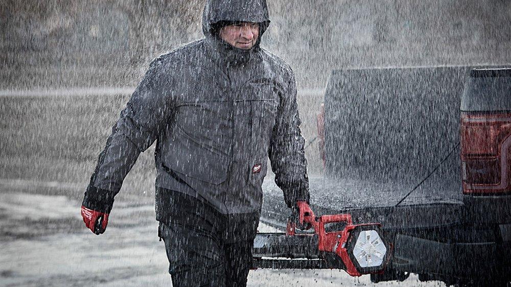 Worker in waterproof rain jacket walks with flashlight through the rain.