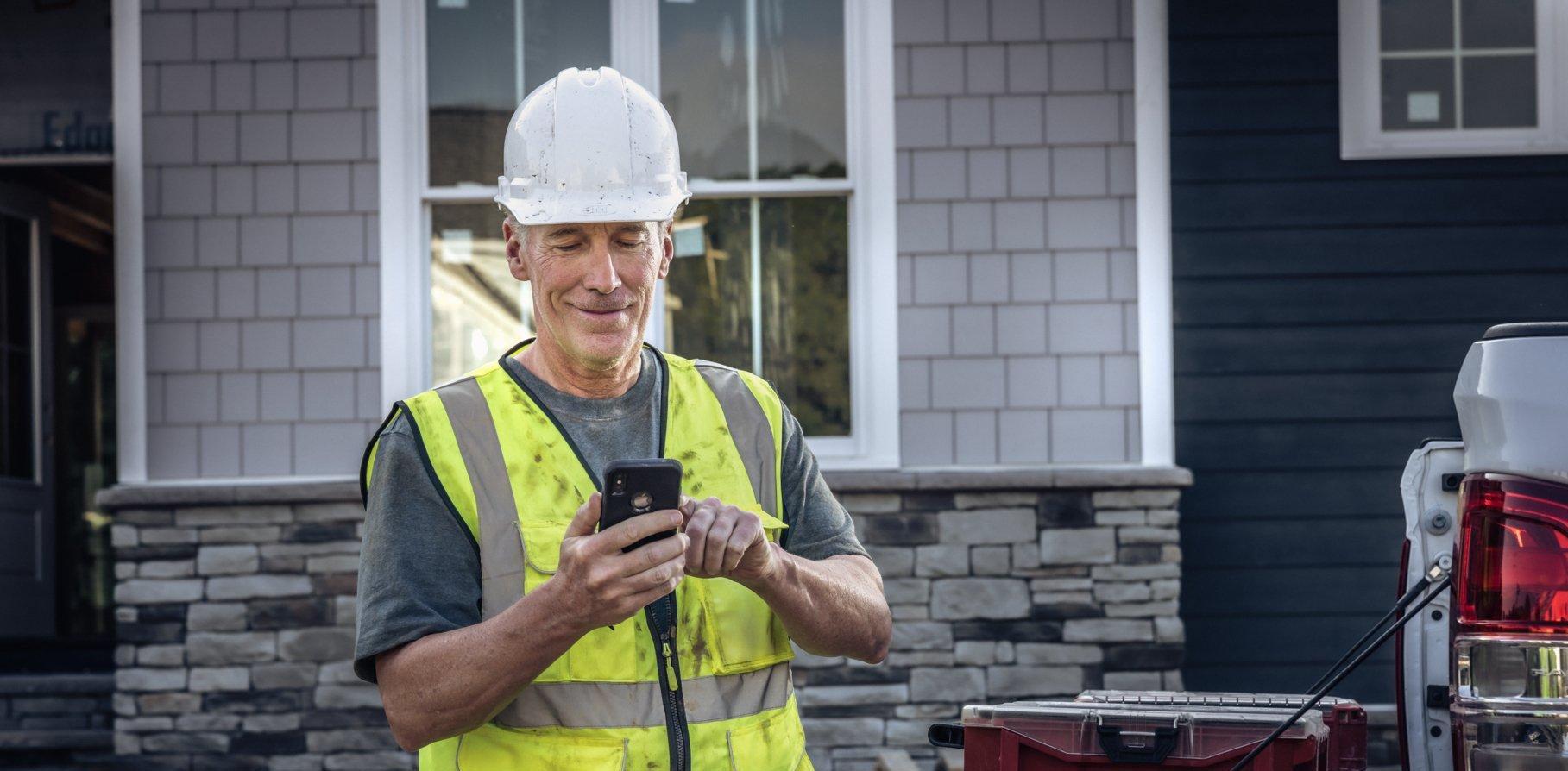 A contractor on a residential build site smiles as he taps on his smartphone.