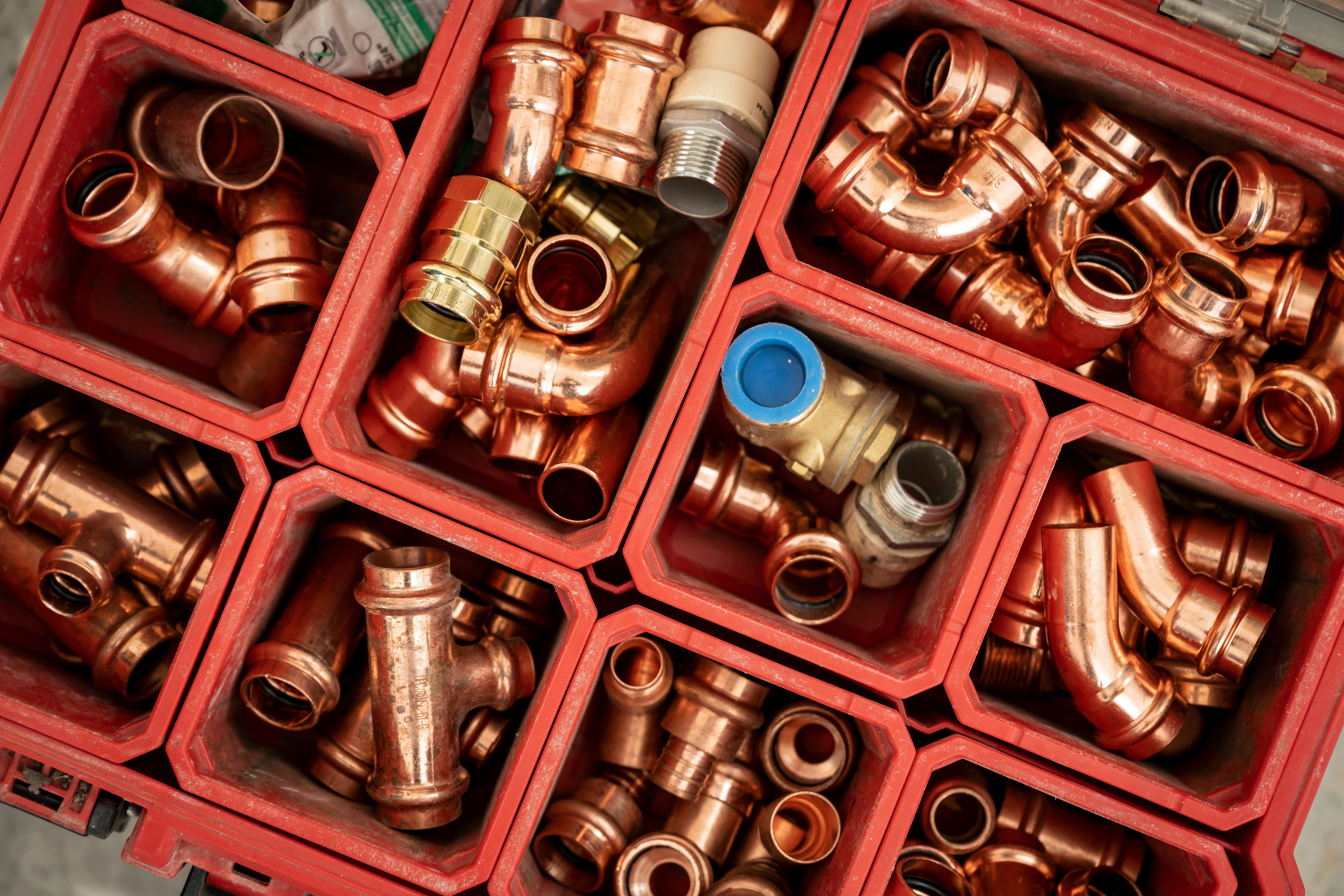 Plumbing parts, pipe, valves and fittings separated in a red toolbox.