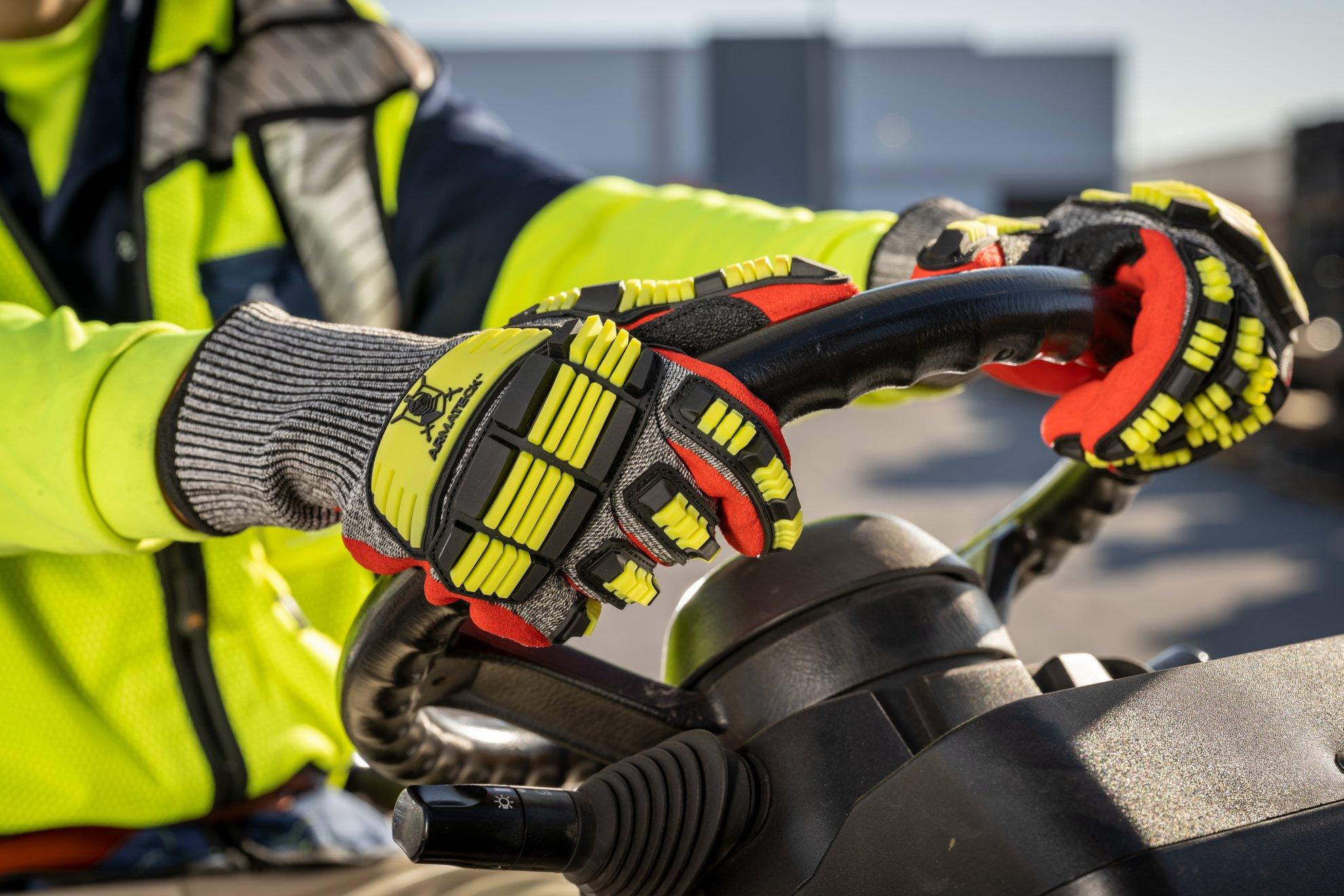 A worker wearing a yellow reflective vest and yellow Armateck safety gloves operates a forklift.