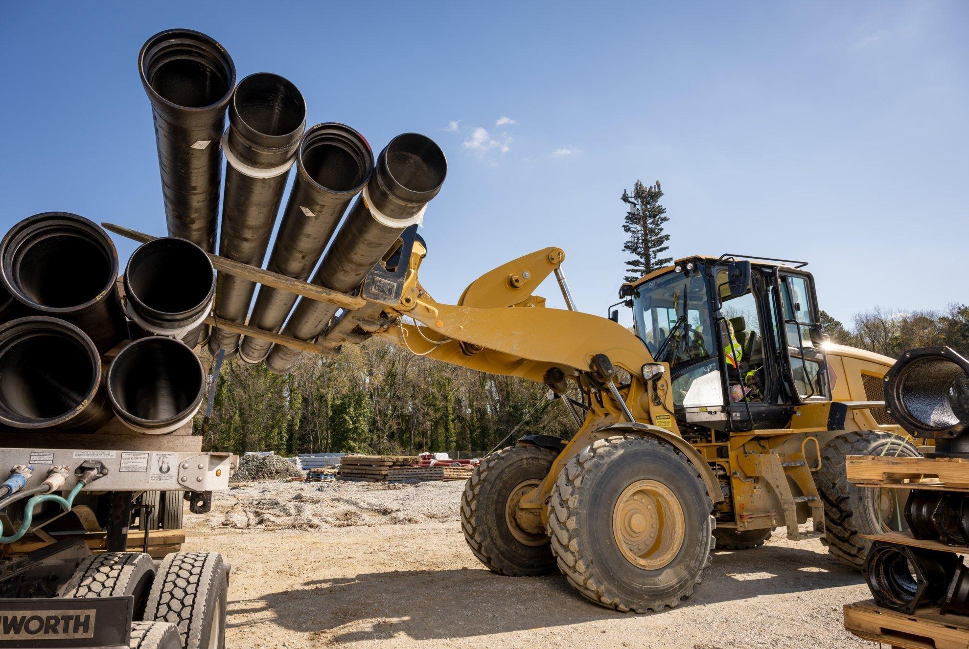 A front-end loader removes industrial pipe from a flatbed on a construction site.