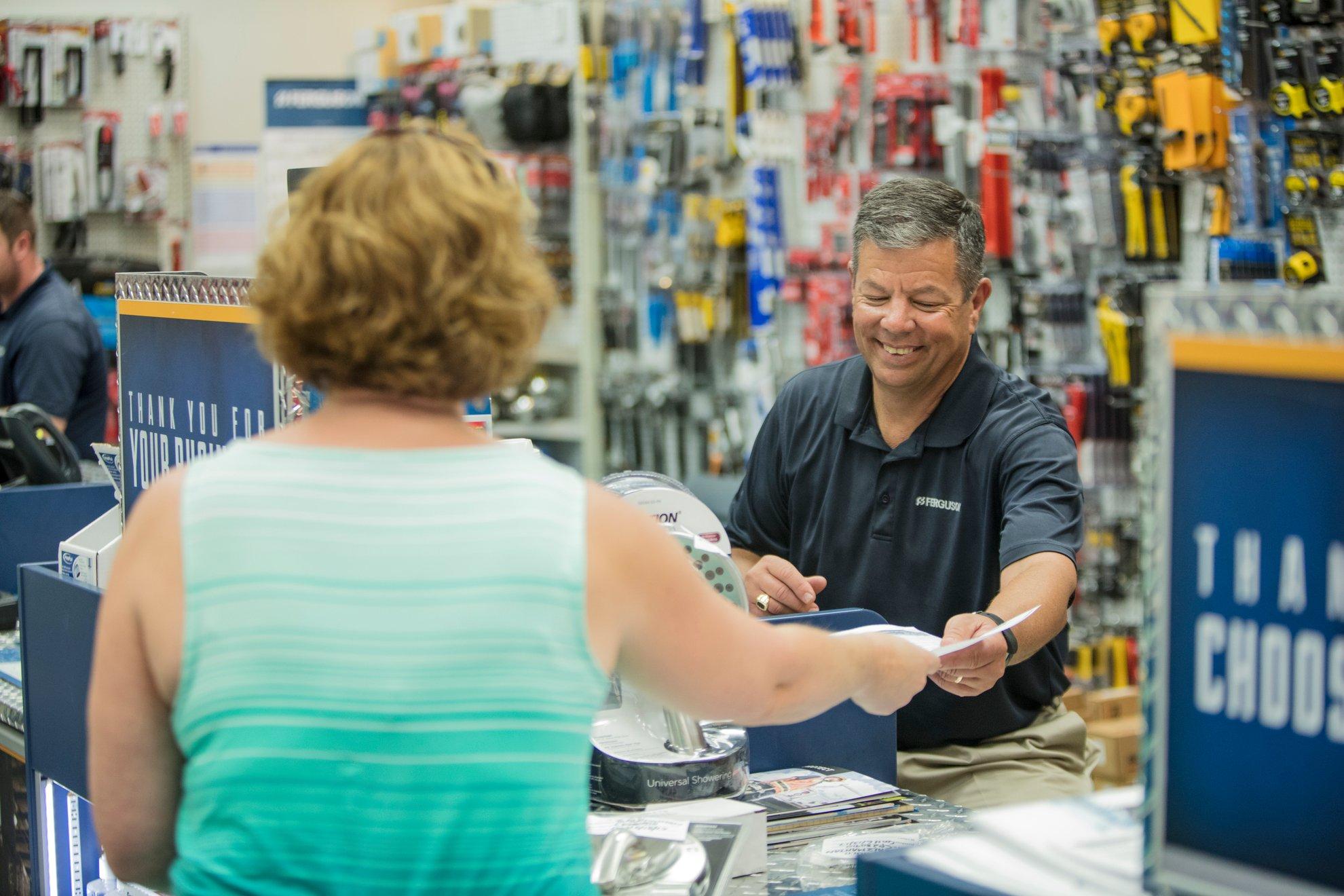 At a Ferguson counter location, a smiling associate behind the counter takes a piece of paper from a customer.