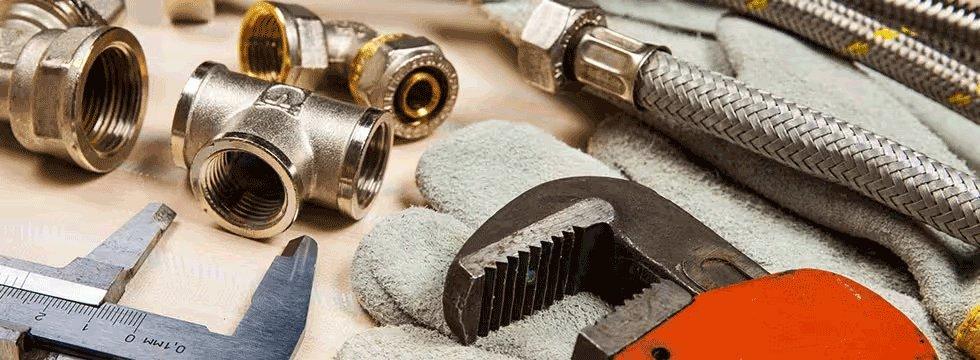 View of plumbing tools on a table, including hoses, pipe fittings, gloves and an open-end wrench.