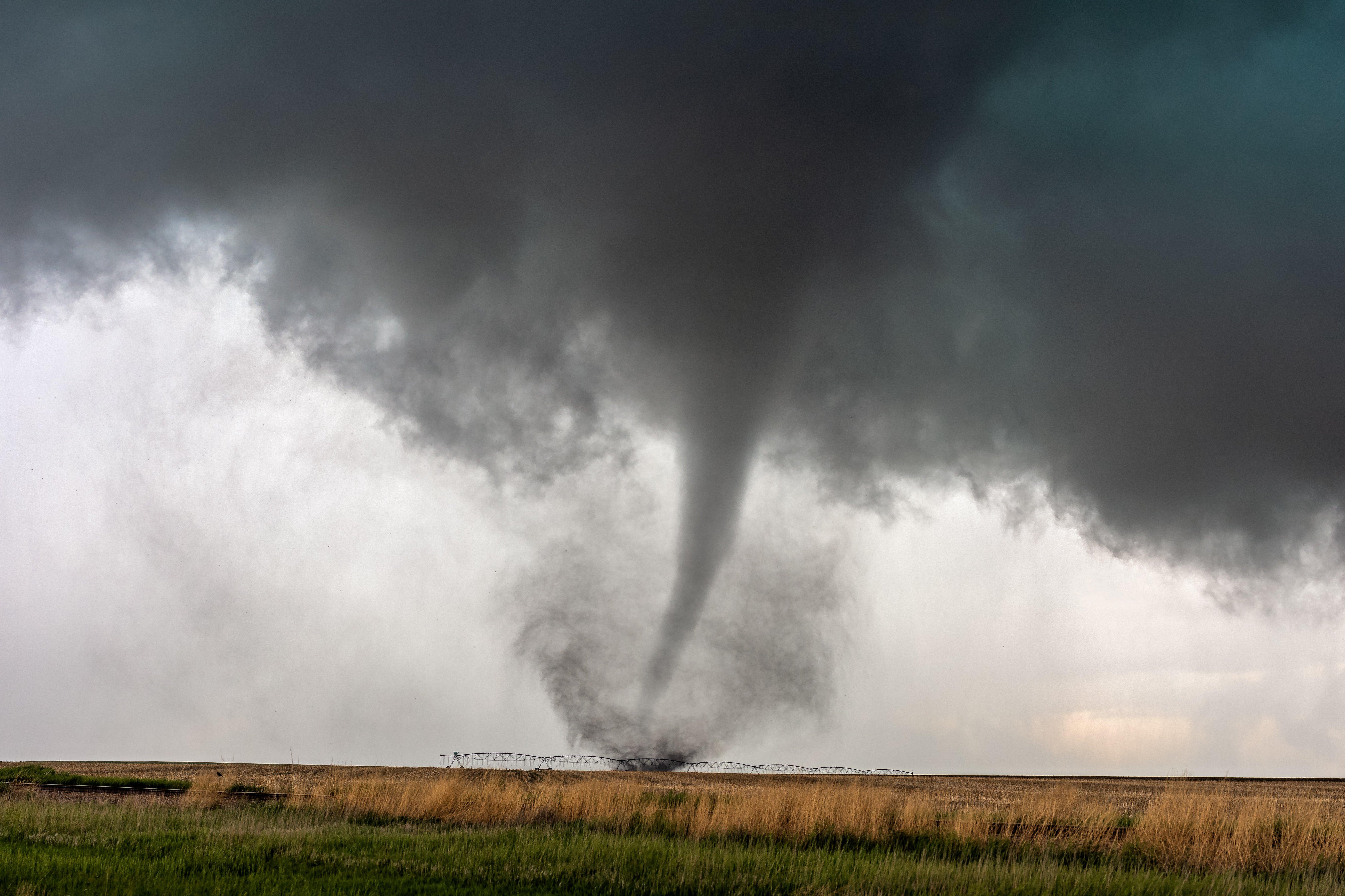A tornado touches down behind an irrigation structure in a field of crops.