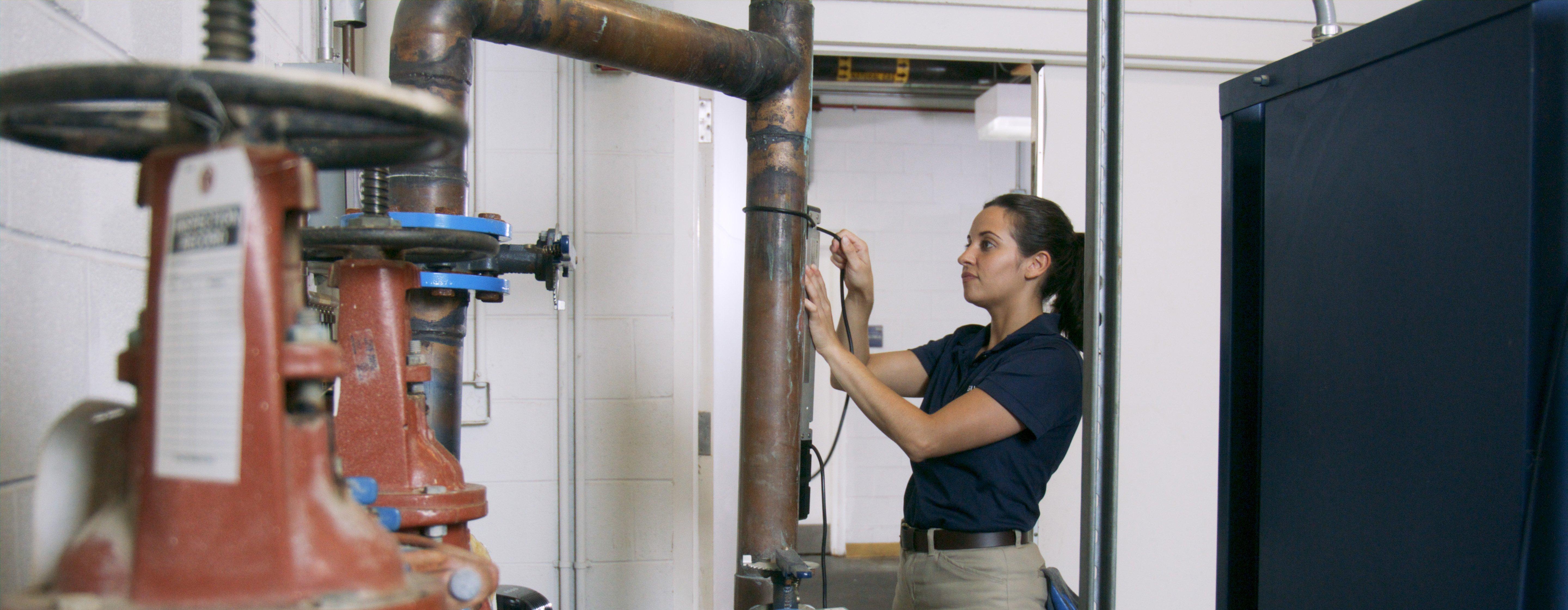 A woman conducting a field audit measures pipe in a mechanical room.