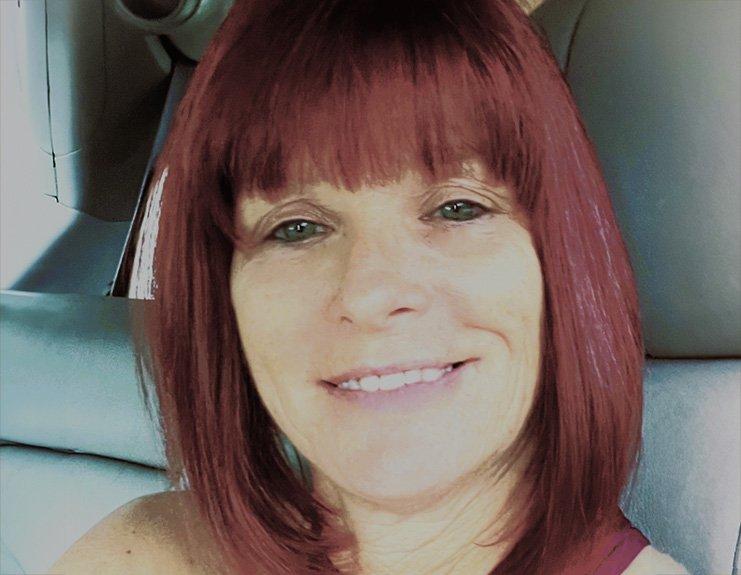 A selfie in a work vehicle depicts Anna Hamilton smiling gently, with shoulder-length red hair neatly trimmed with bangs.