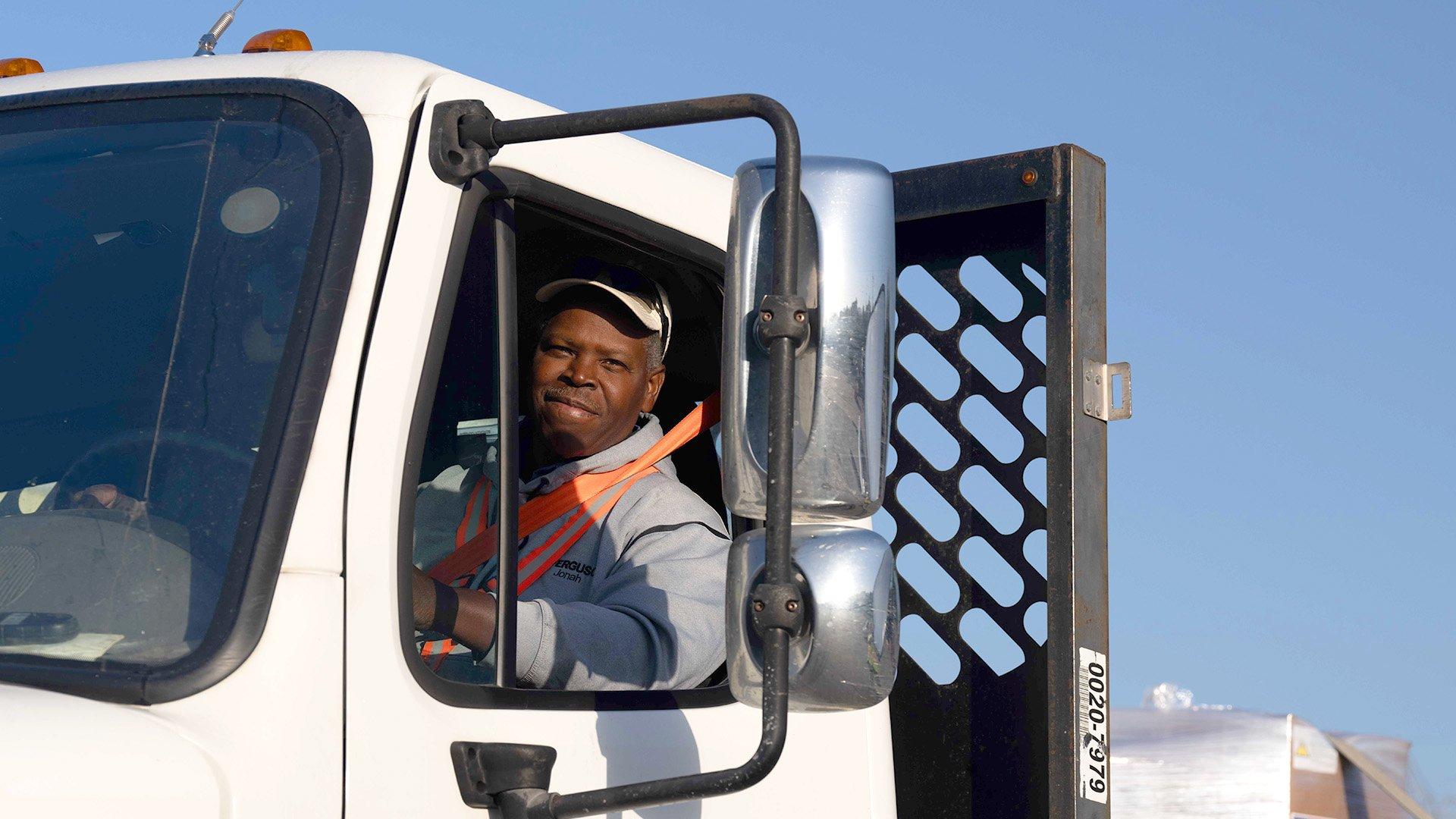 A delivery driver sits behind the wheel of truck and smiles.