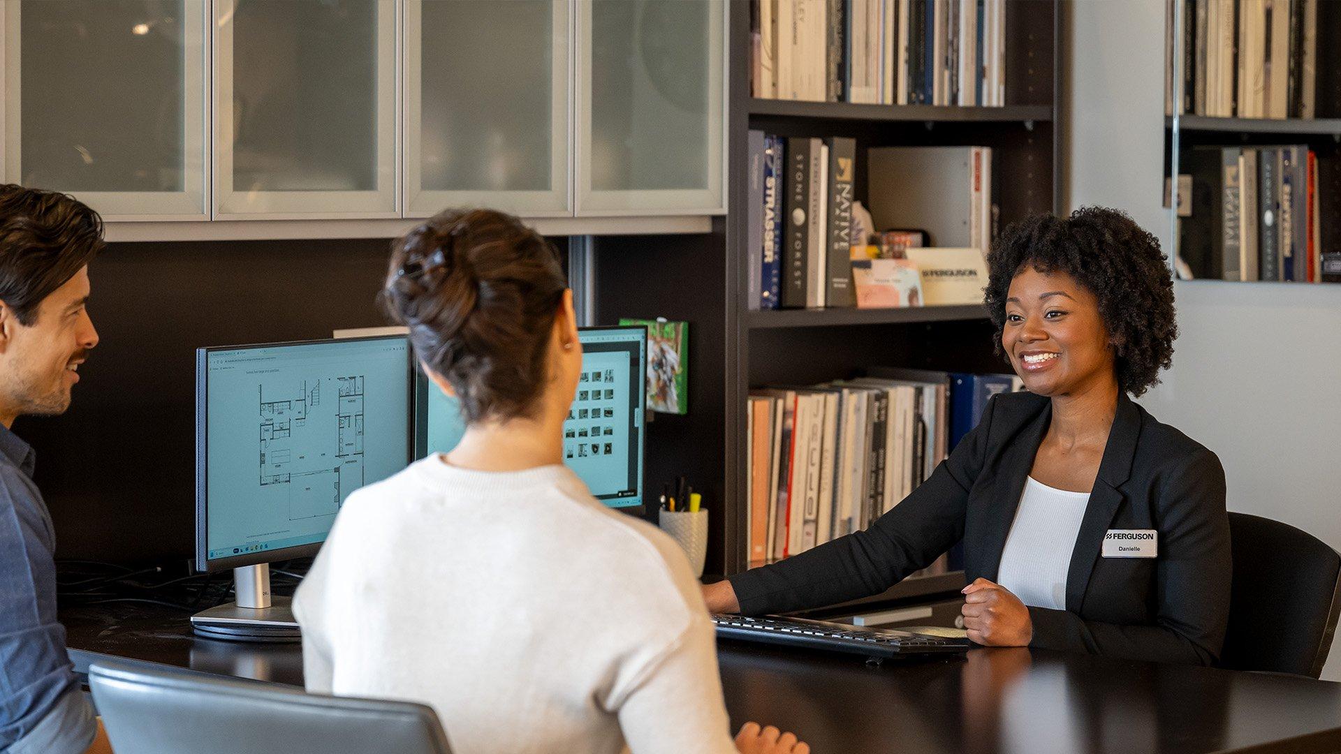 A man and woman sit across the table from a employee sitting at her computer.