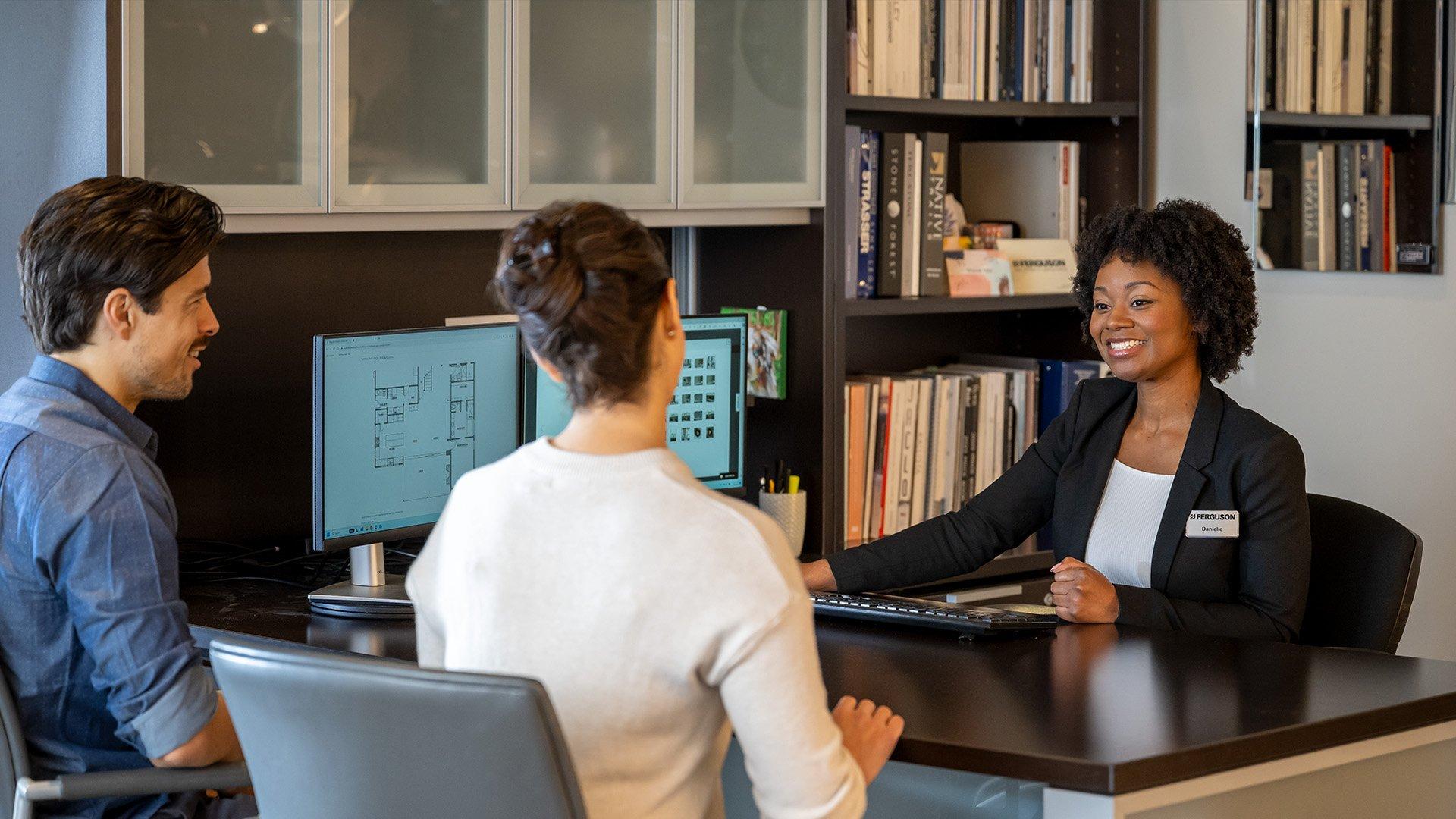 A man and woman sit across the table from a employee sitting at her computer.