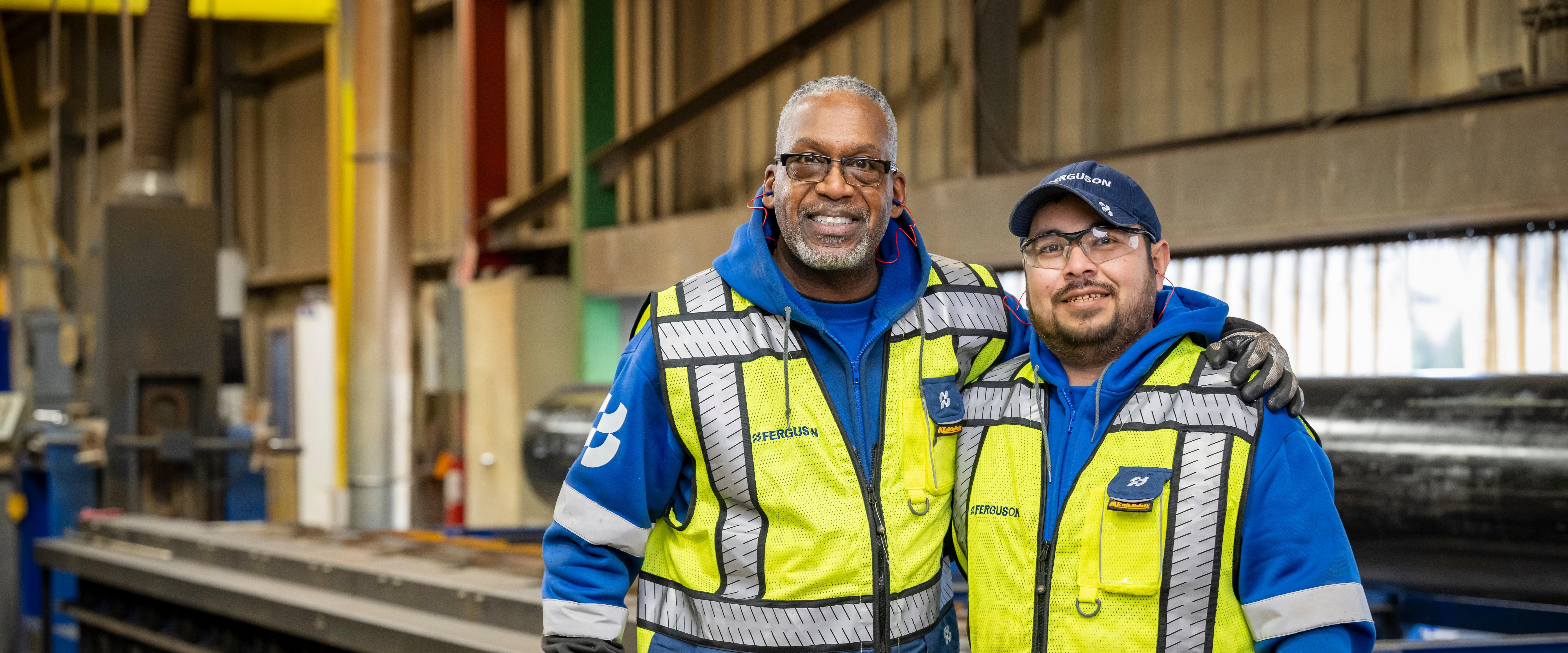 Two Ferguson employees in yellow safety vests stand together and smile at the camera.