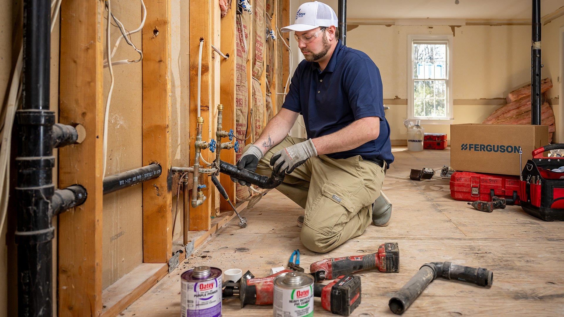 Plumber installing ABS pipe in residential home with Milwaukee tools and Ferguson box in the background.