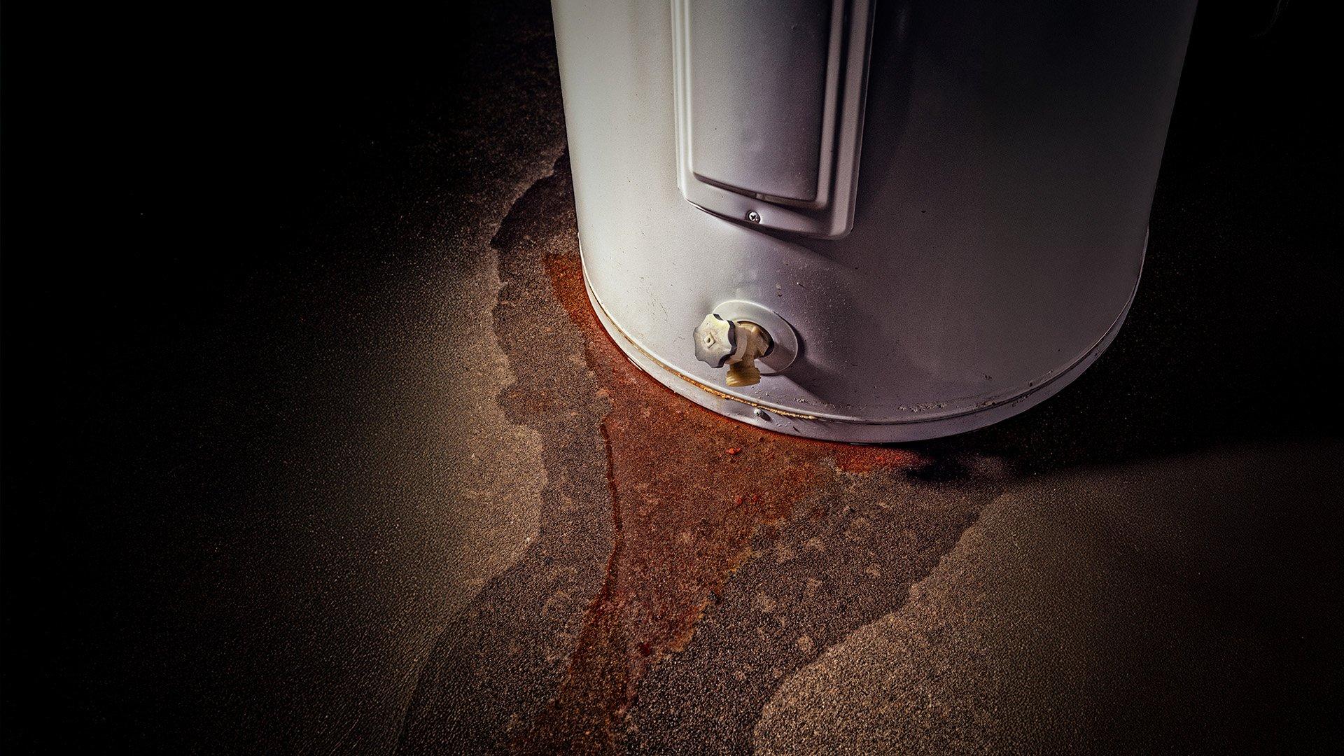 Close up image of bottom of water heater that is leaking water onto floor. 