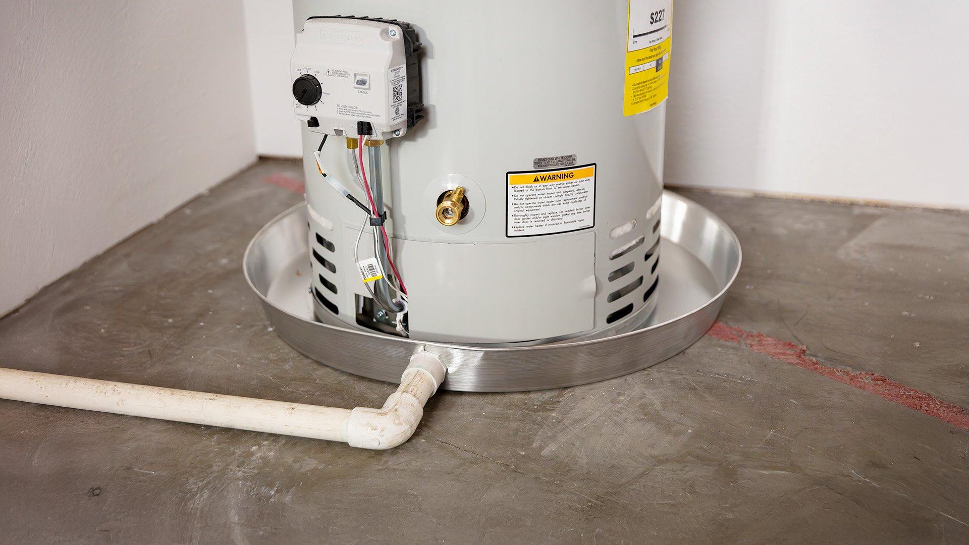 Water heater drip pan underneath residential gas water heater on concrete floor.