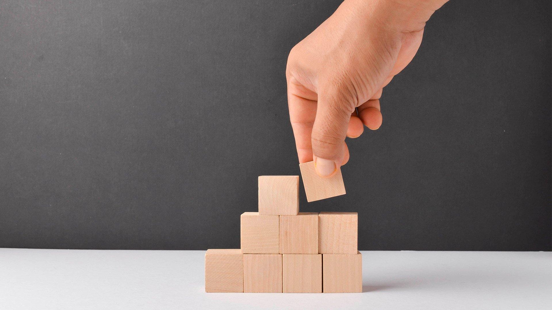 Close up image of hand adding wooden blocks to a tower. 