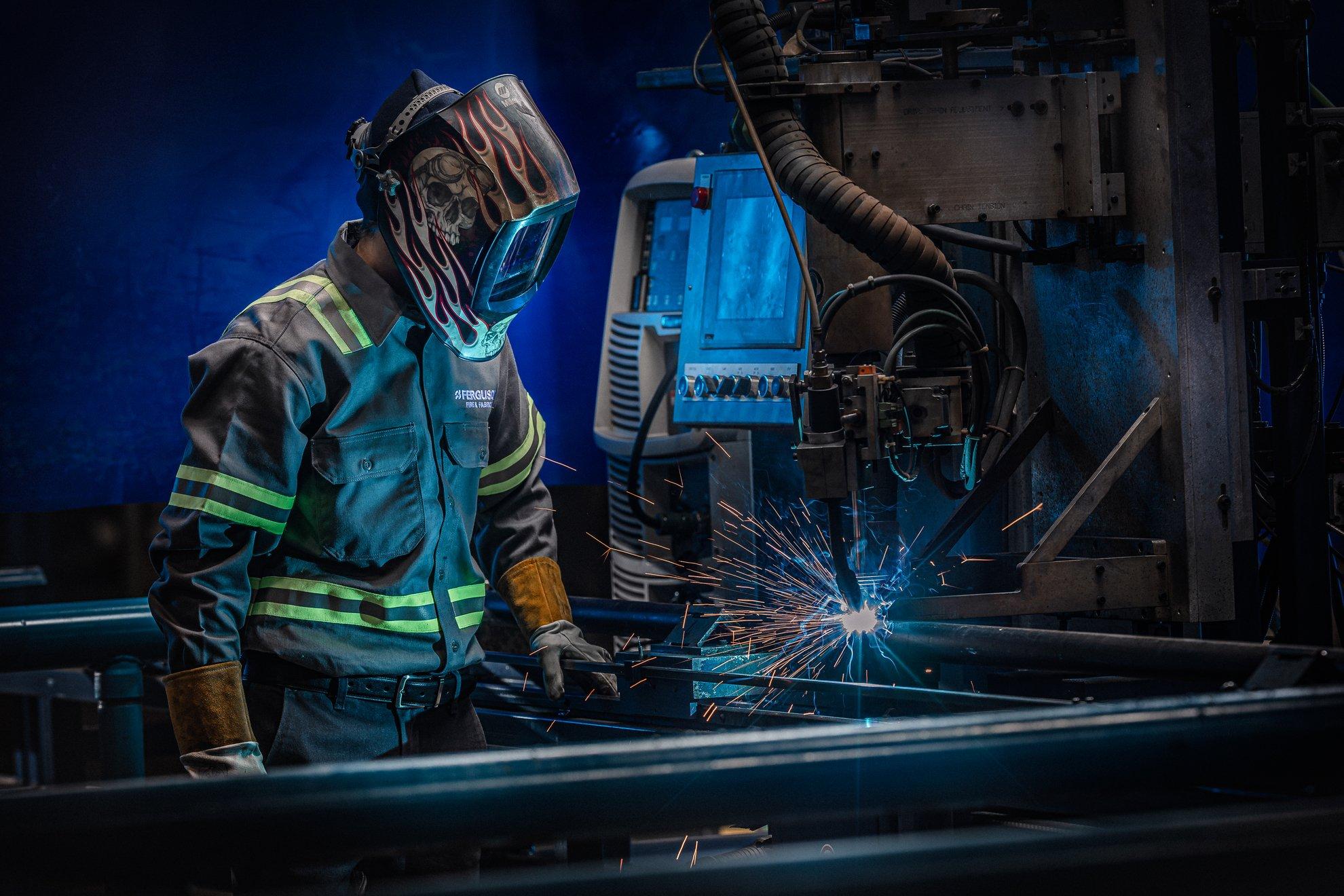 A Ferguson associate in full PPE stands near a machine cutting pipe.