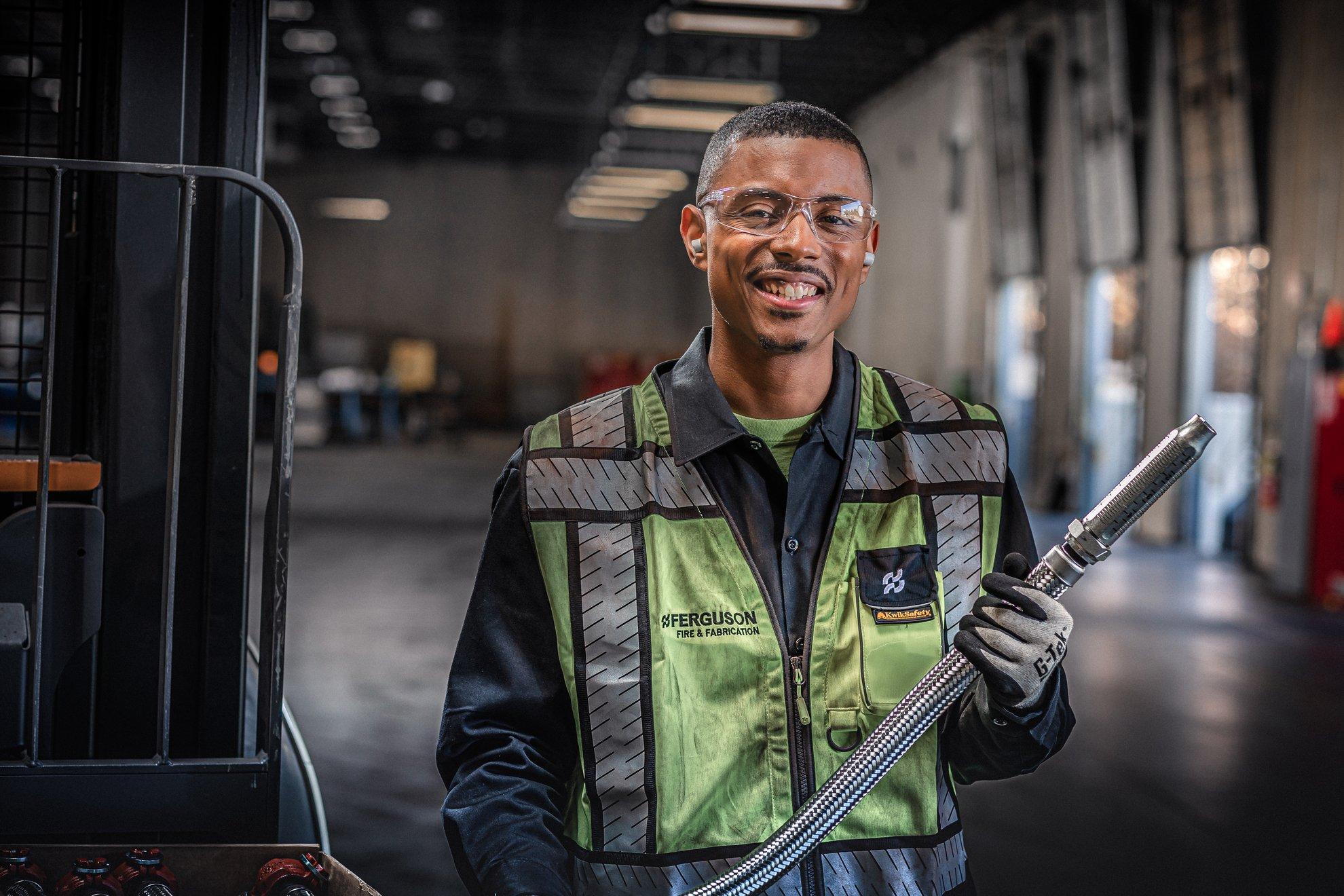 An associate in safety glasses and a reflective Ferguson vest holds a stainless steel hose.
