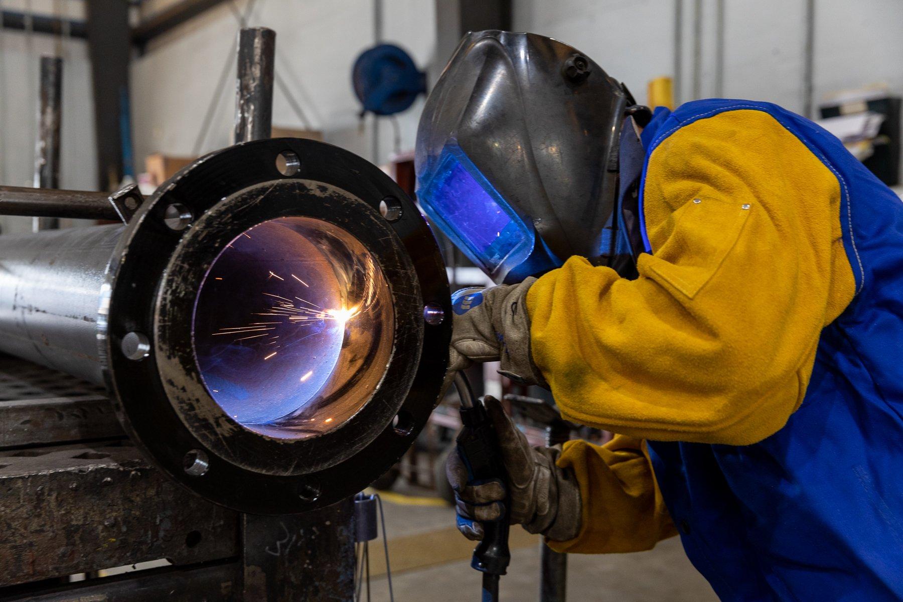 A welder in full personal protective equipment cuts a pipe.
